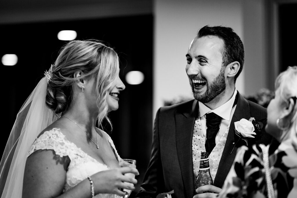 Bride and groom sharing a laugh with drinks during the reception, black and white, Cheshire wedding photographer