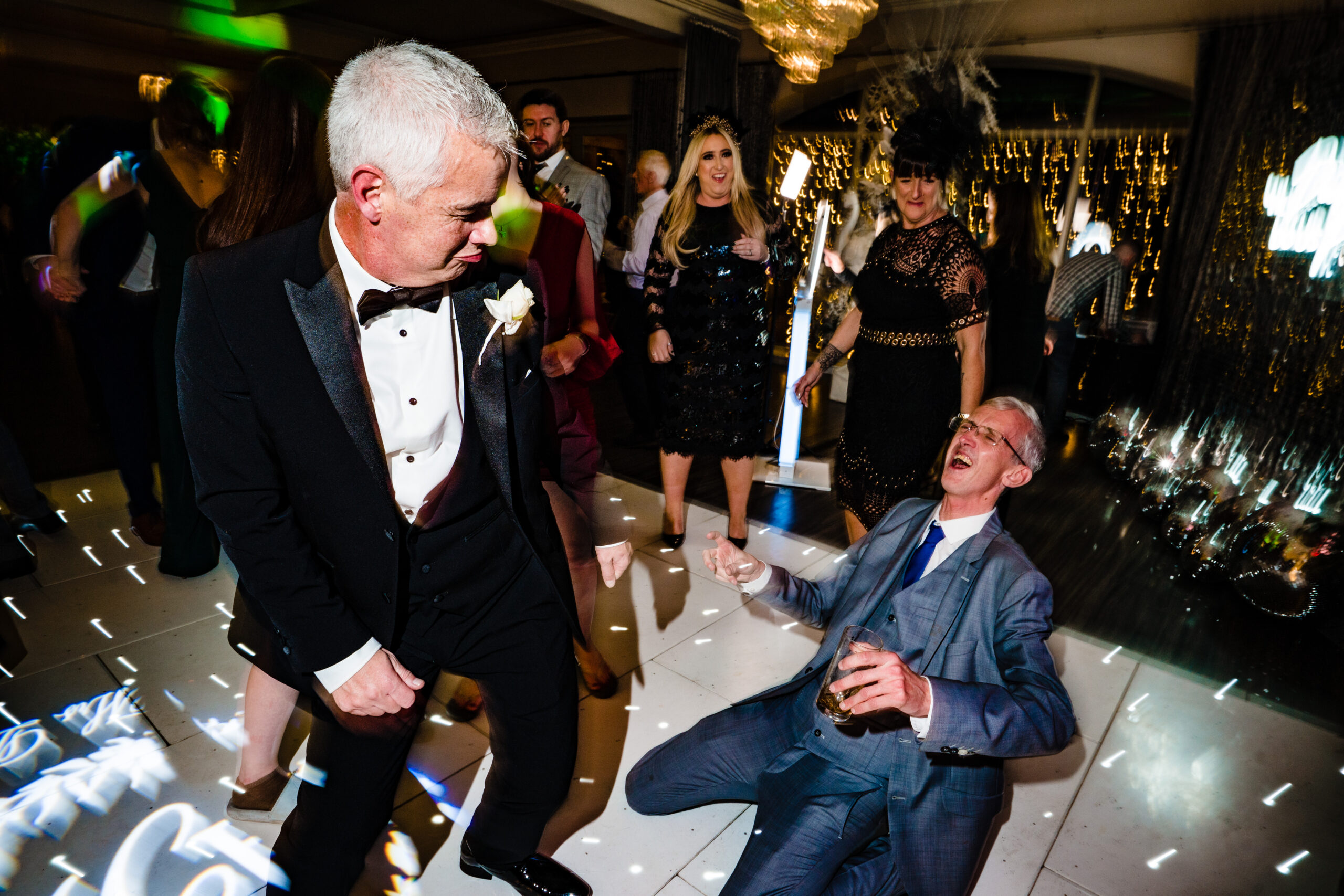 A guest in black tie dancing while another laughs from the dance floor at Merrydale Manor