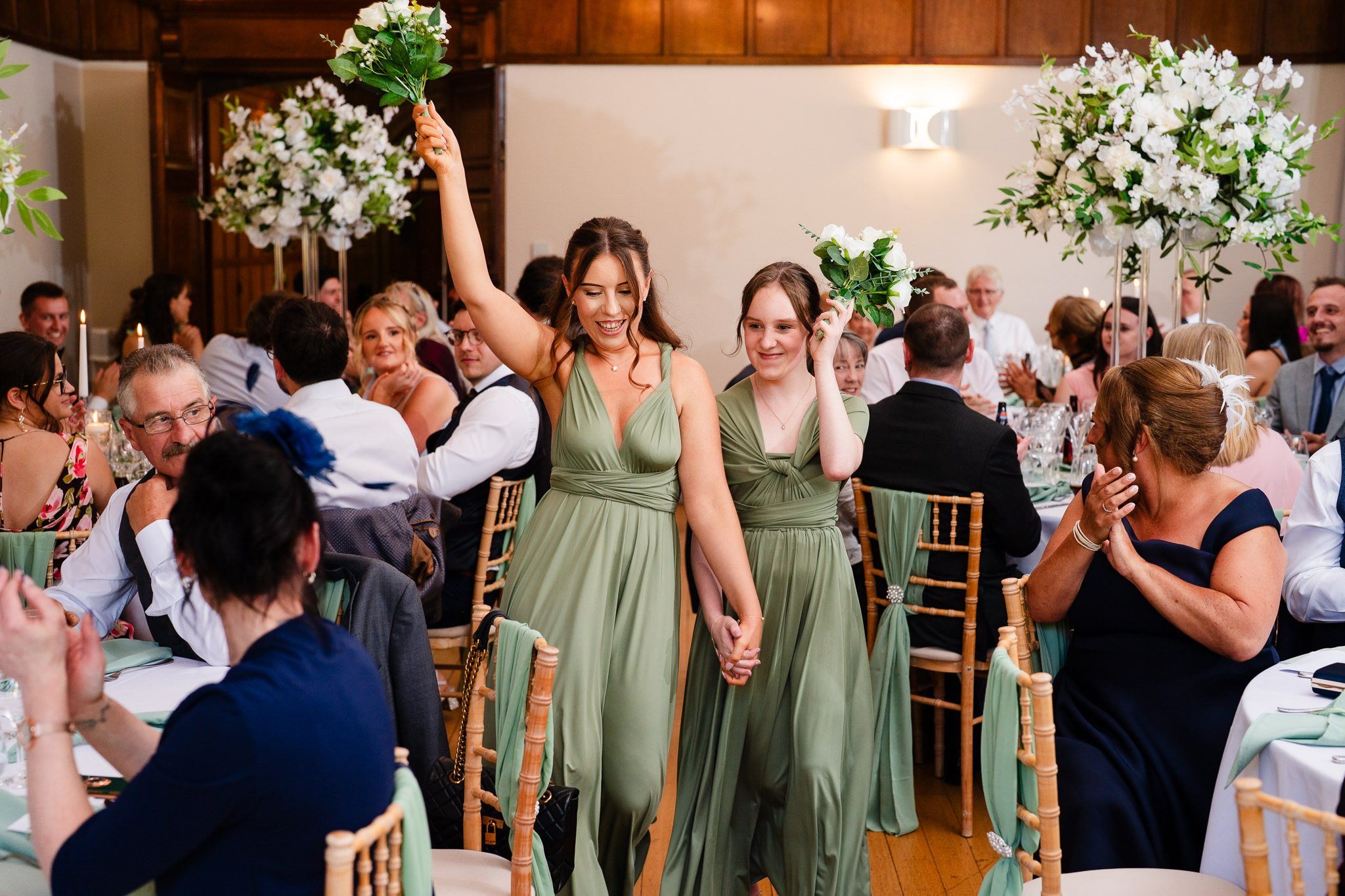 Bridesmaids arriving into the reception room with bouquets raised, guests clapping either side