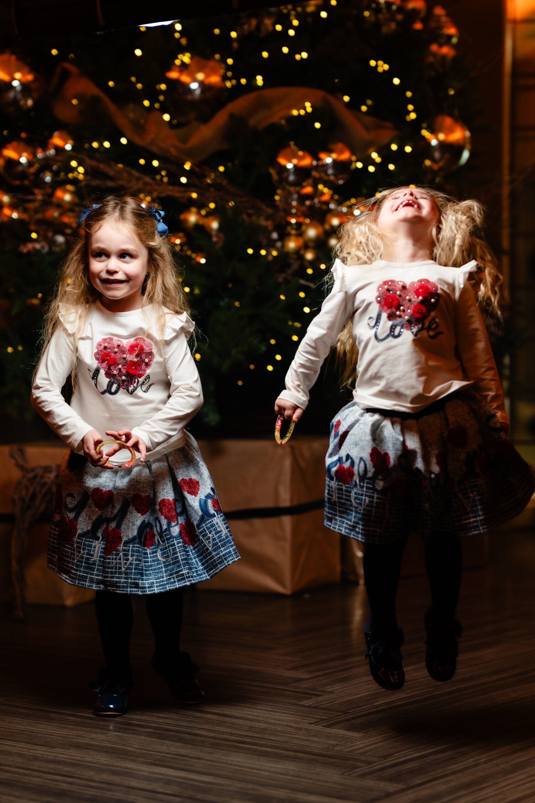Two small guests in matching Christmas jumpers in front of the tree, one mid jump, Colshaw Hall winter wedding