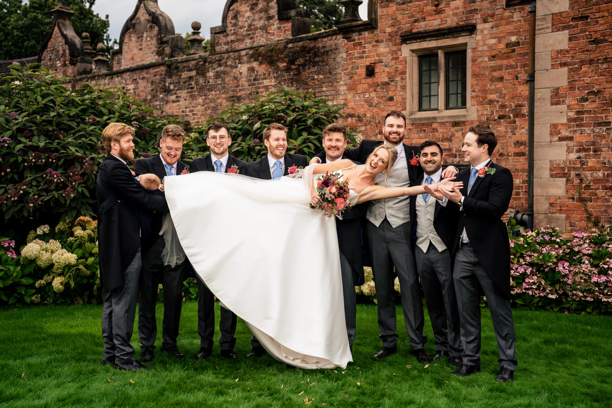 Groomsmen fanning out the bride’s dress on the lawn at Dorfold Hall, Dorfold Hall wedding photographer