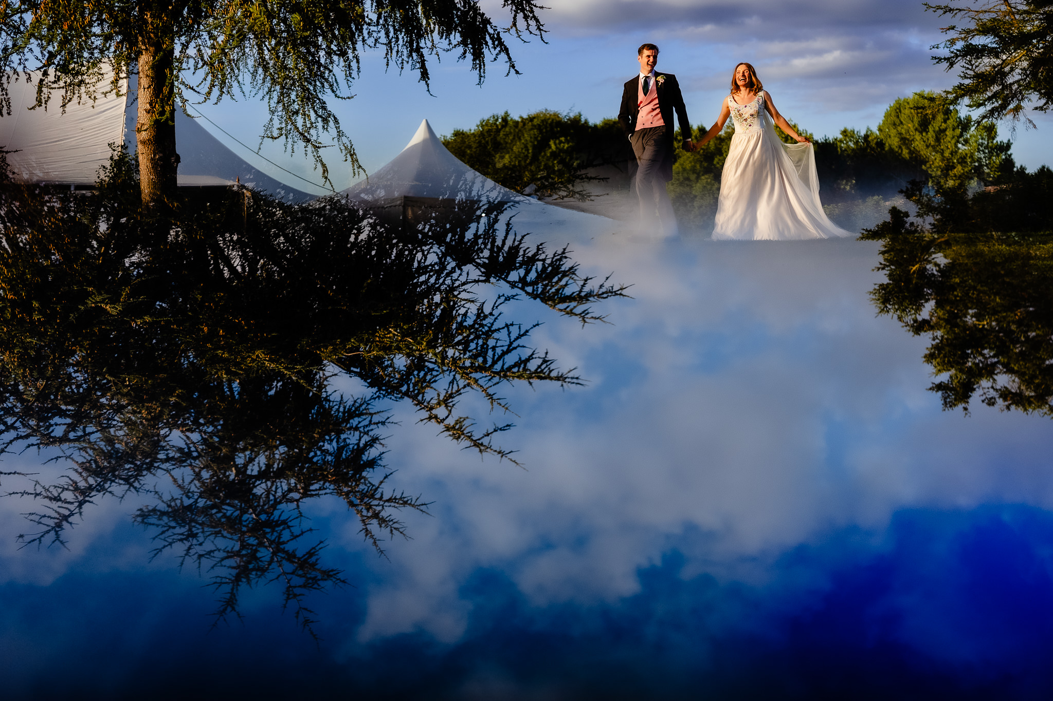 Bride and groom reflected upside down in still water beside the marquee, Dorset marquee wedding photographer