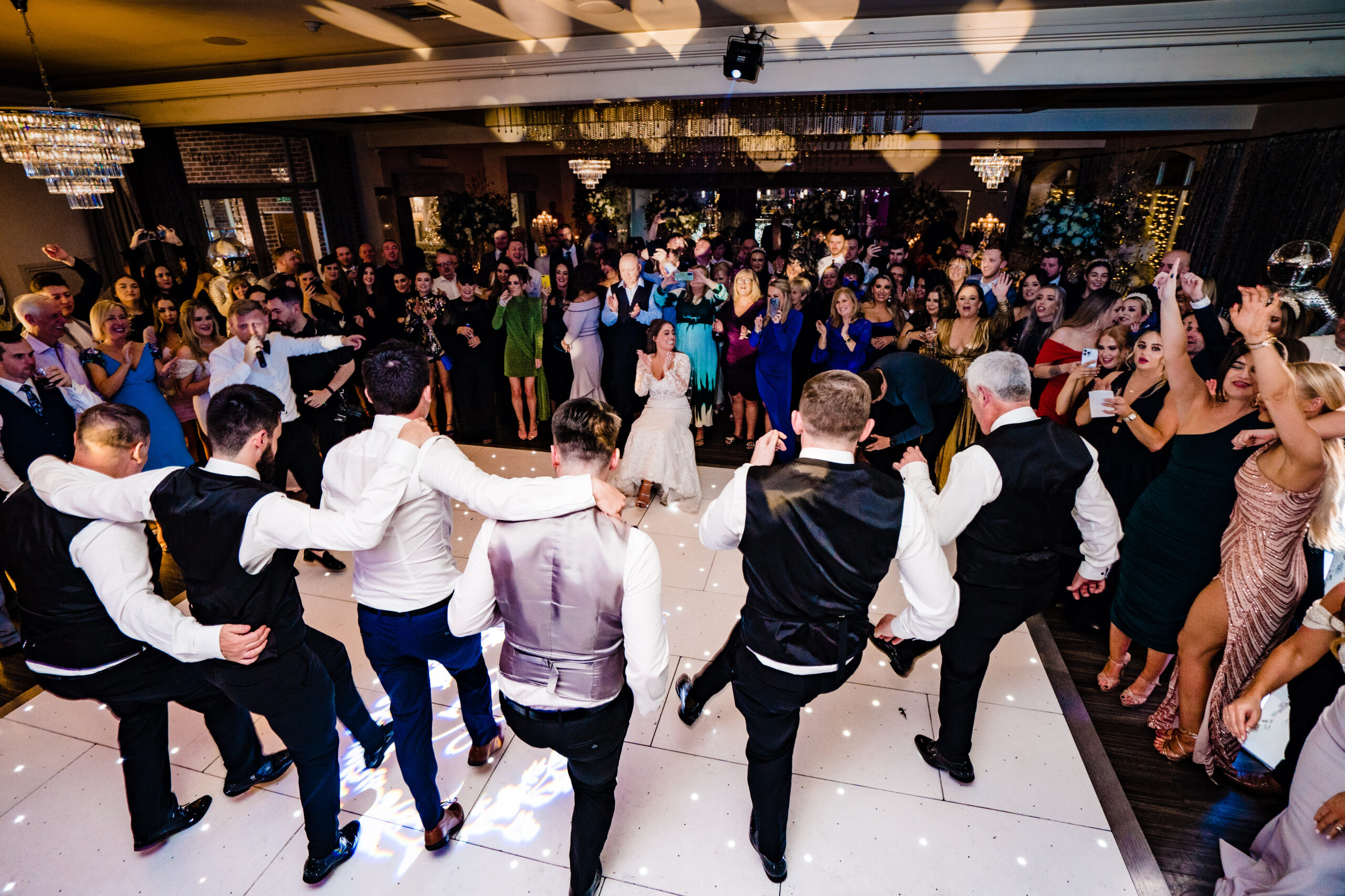 The lads dancing with arms linked and legs kicking in front of a packed room at Merrydale Manor