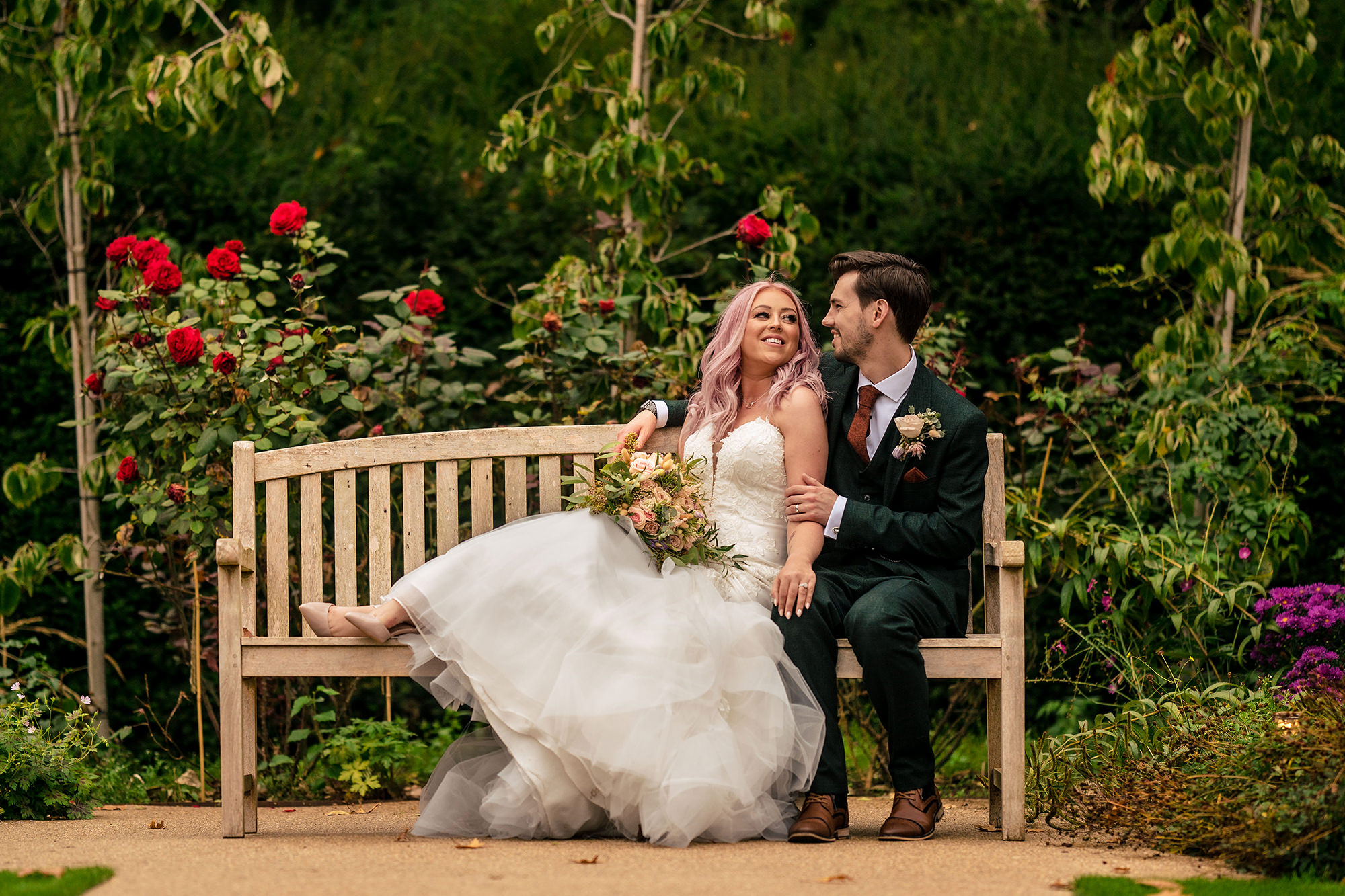 Bride and groom sharing a quiet moment on a bench among the roses at Standon Hall