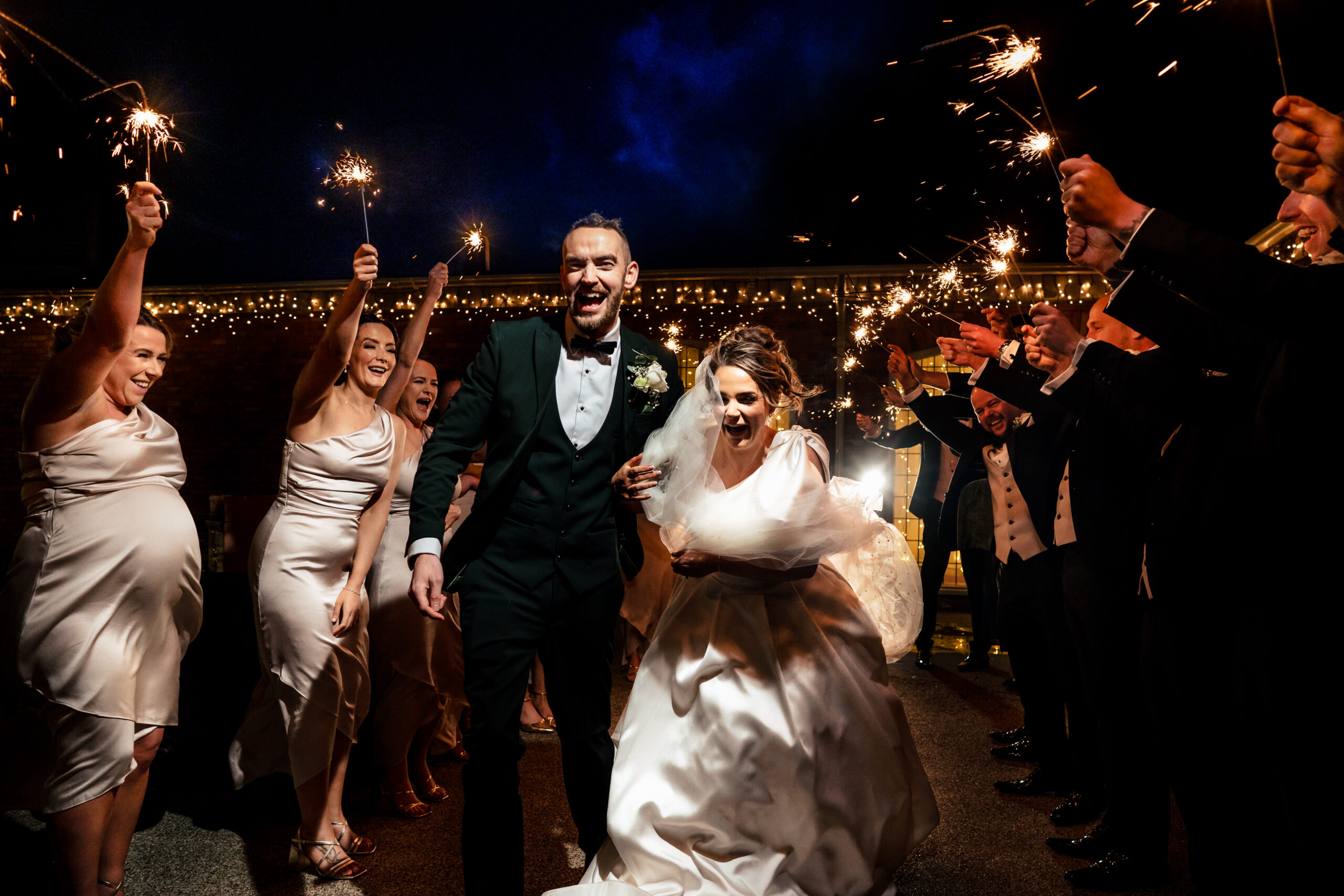 Georgia and Joe running through a tunnel of sparklers held by their guests