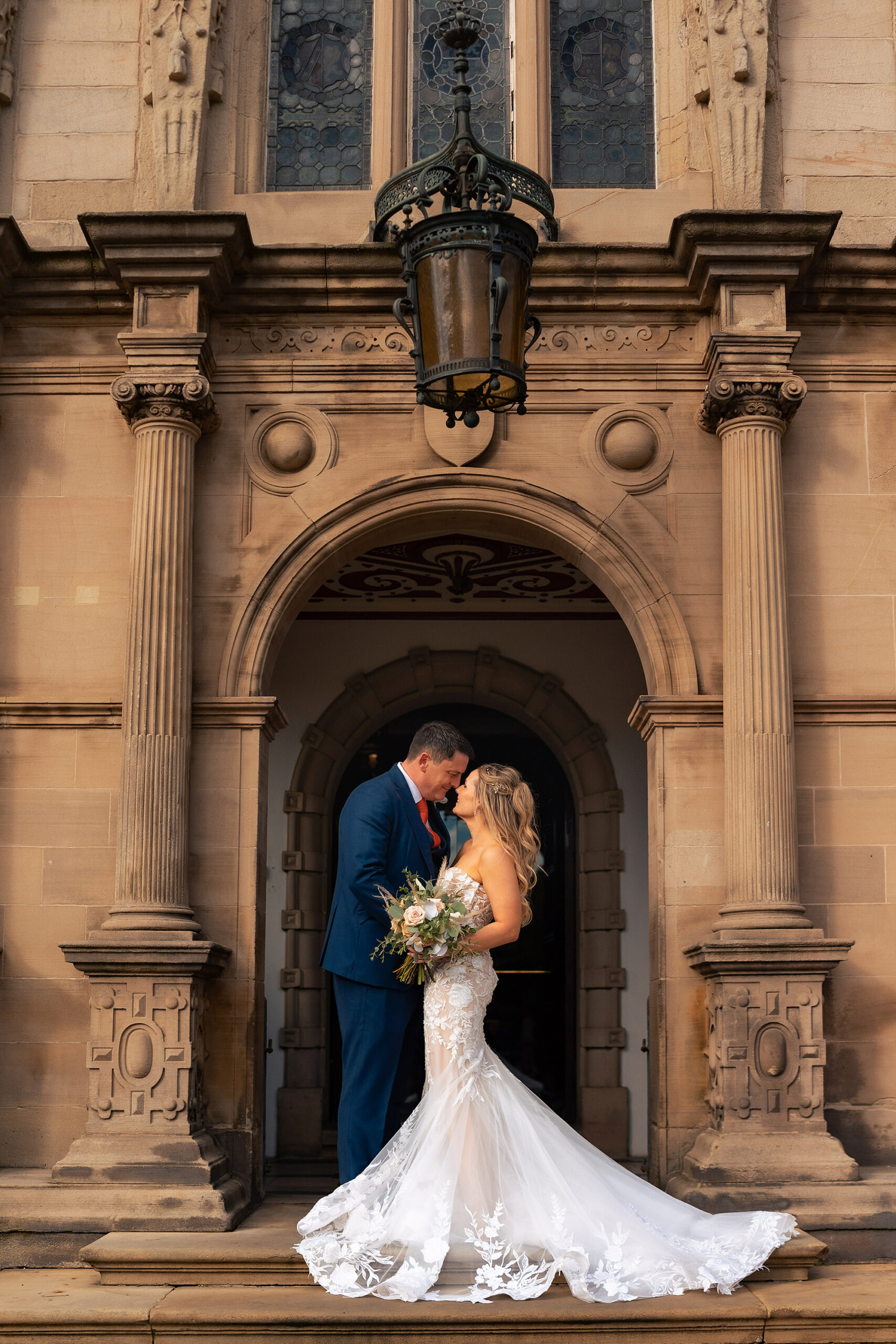 The couple framed in the stone archway at Crewe Hall with the bride’s train spread out across the step