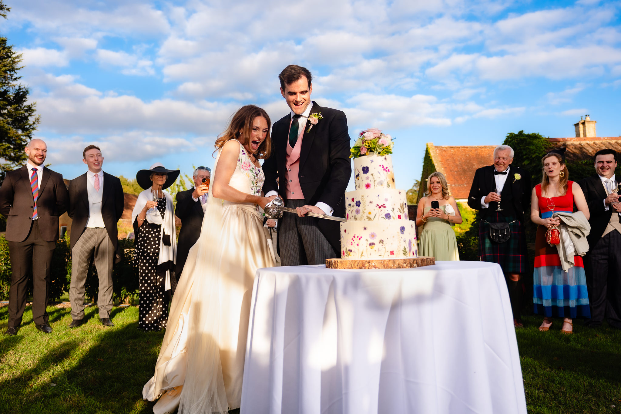 Bride and groom cutting their iced flower wedding cake in front of their guests