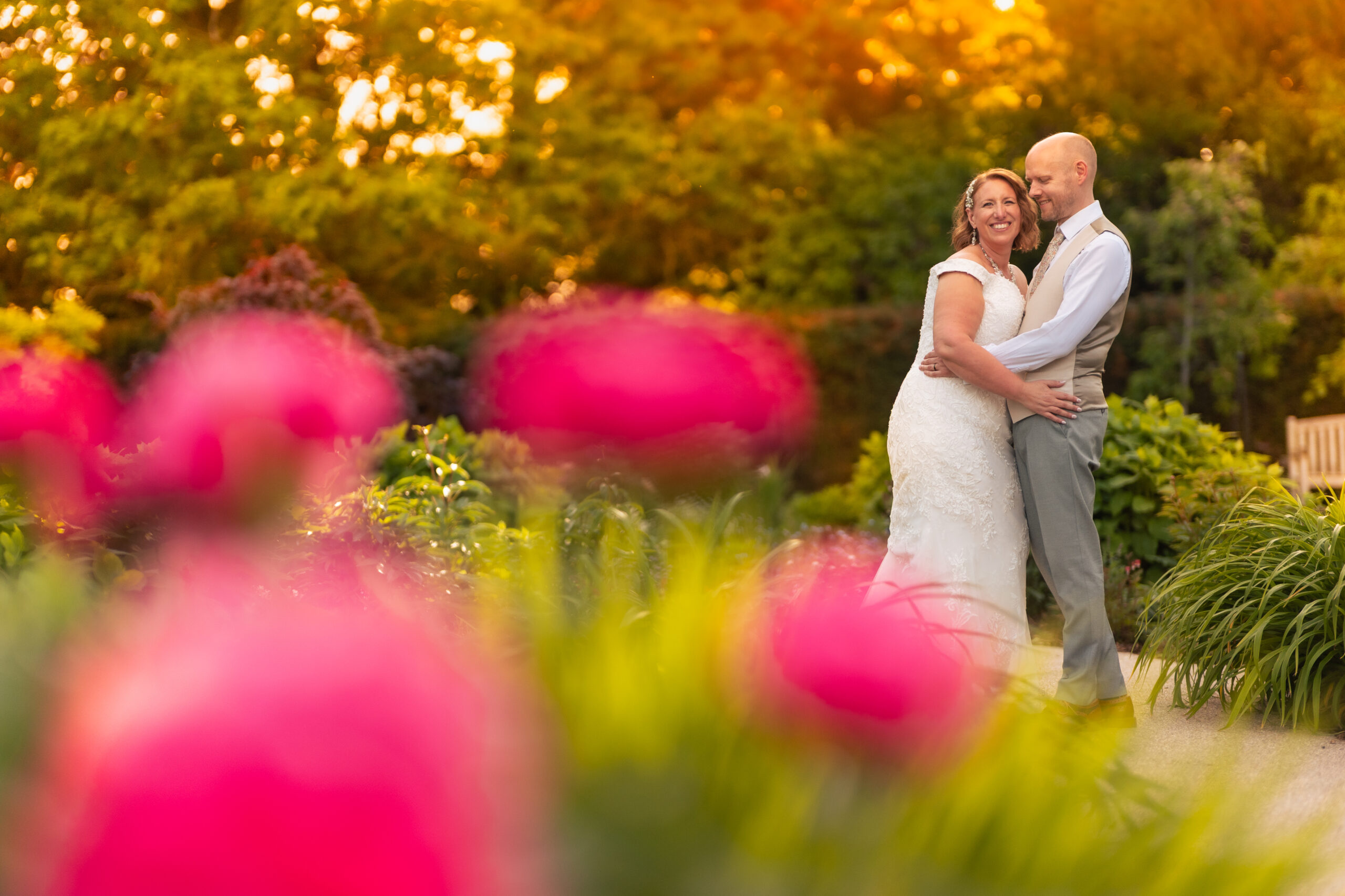 Bride and groom embracing among pink flowers in the Salt House gardens at golden hour