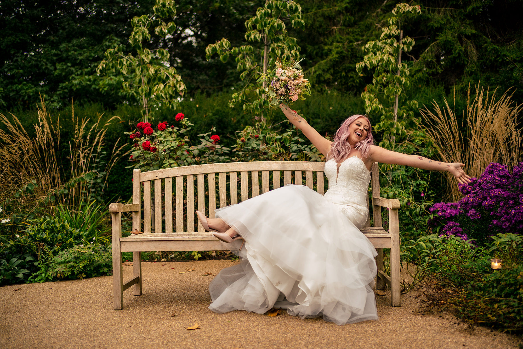 Bride laughing with her arms open on a garden bench at Standon Hall