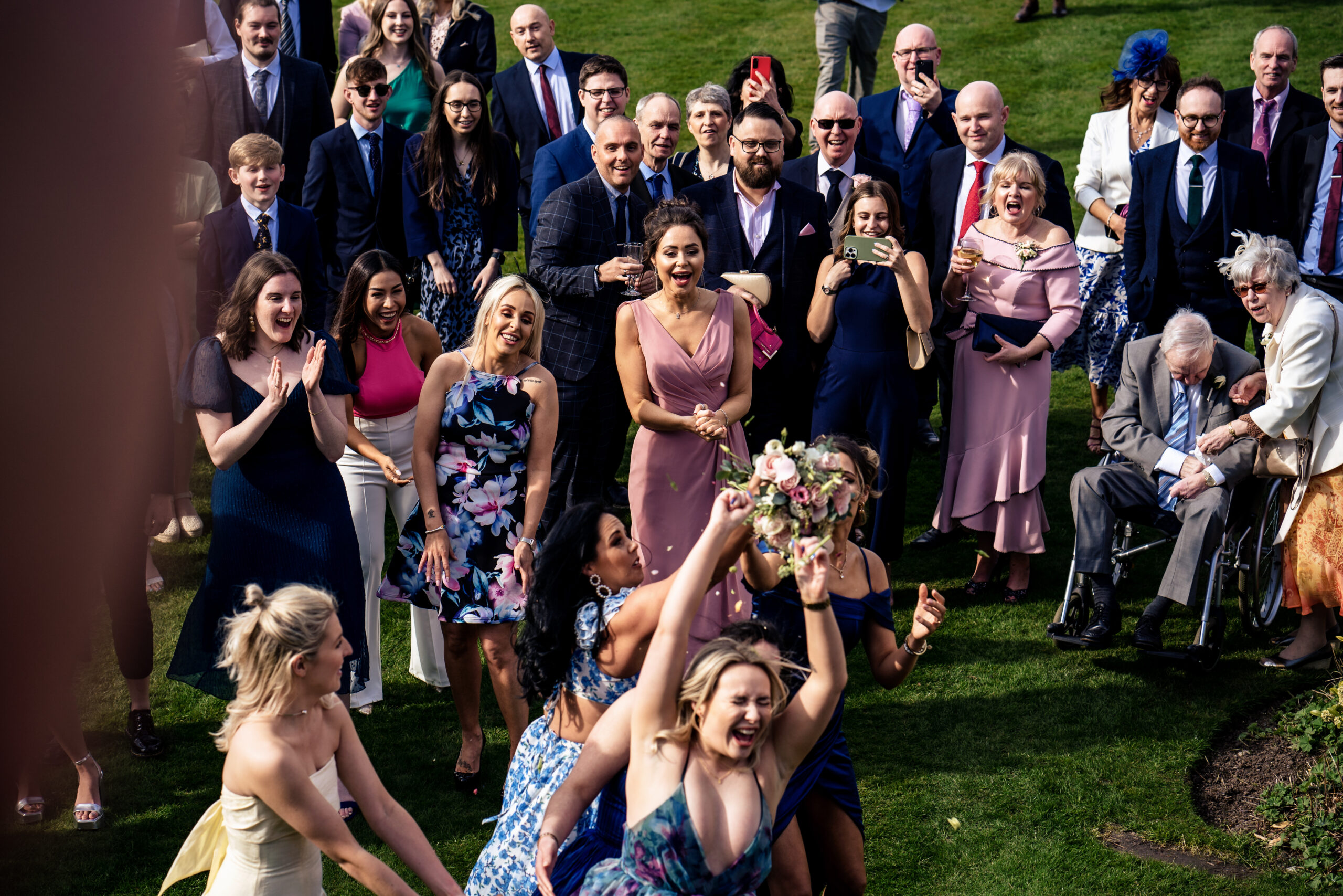 Guests reaching for the bouquet as it comes down, with the crowd behind them cheering
