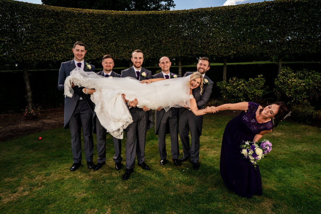 Groomsmen lifting the bride horizontally while a bridesmaid doubles over laughing, Merrydale Manor wedding photographer