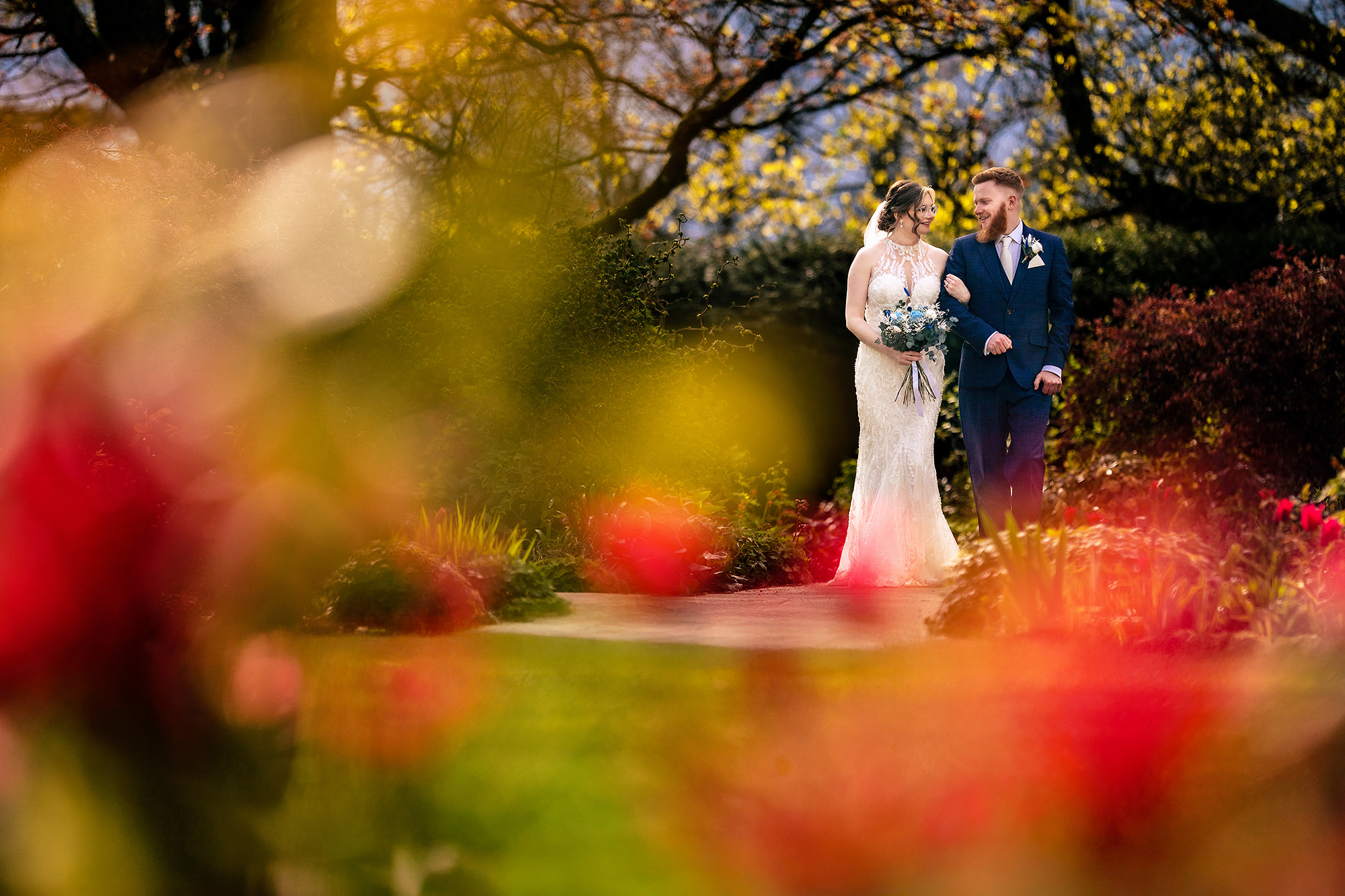 Bride and groom pictured through blurred red autumn foliage in the garden, Salt House wedding photographer