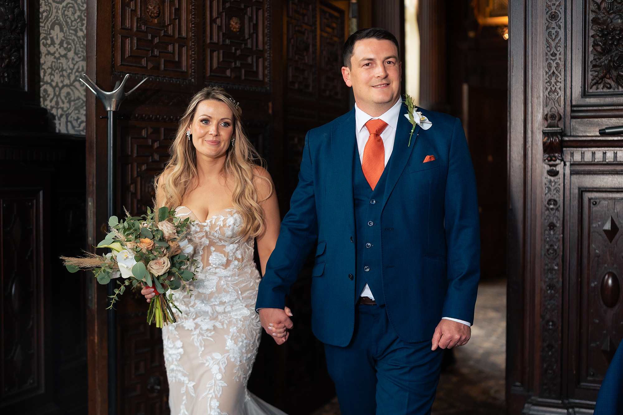 The bride and groom walking in hand in hand through heavy carved doors for their wedding breakfast at Crewe Hall