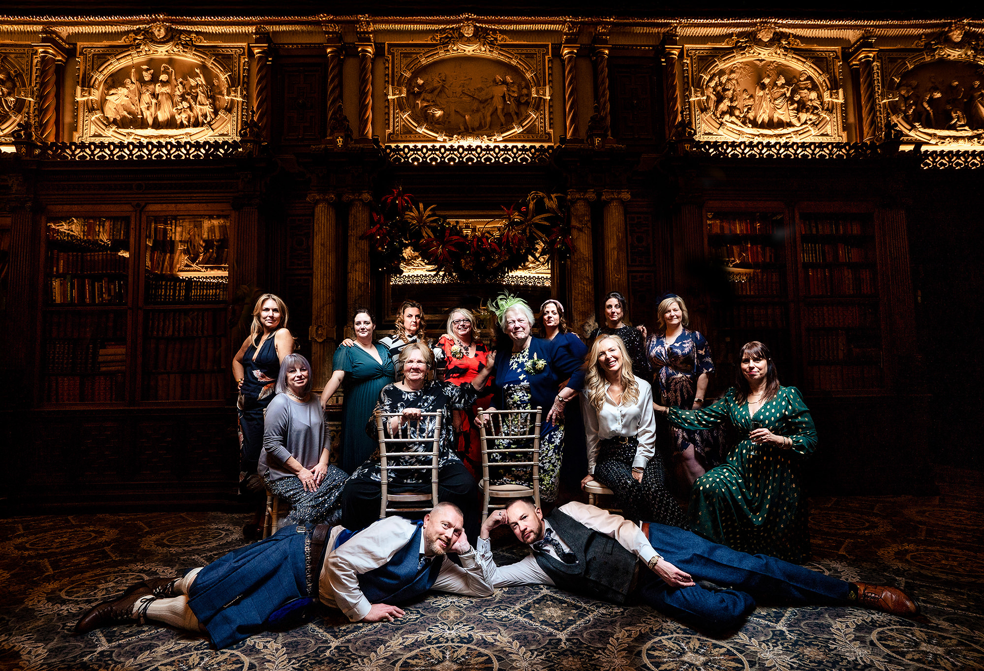 John and Neill lying on the floor for a playful group photo with family in the library at Crewe Hall