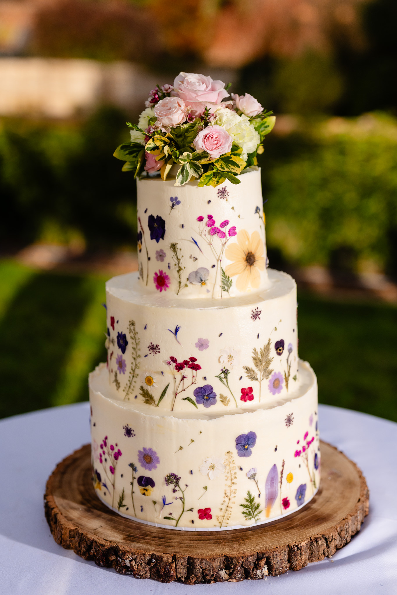 Three tier wedding cake covered in hand piped iced flowers, on a wooden slice