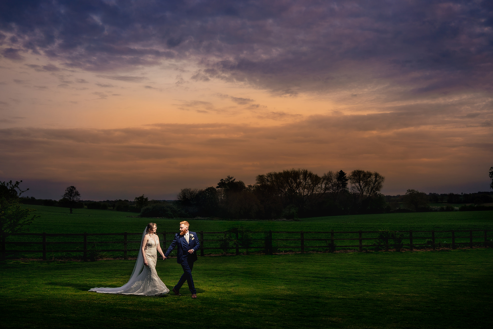 Patrick and Laurel walking hand in hand across the fields at dusk, Staffordshire wedding photographer