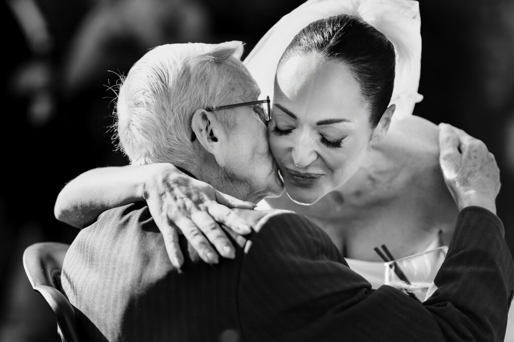 Black and white of an older guest kissing Kim's cheek in a tight hug, Swancar Farm wedding photographer