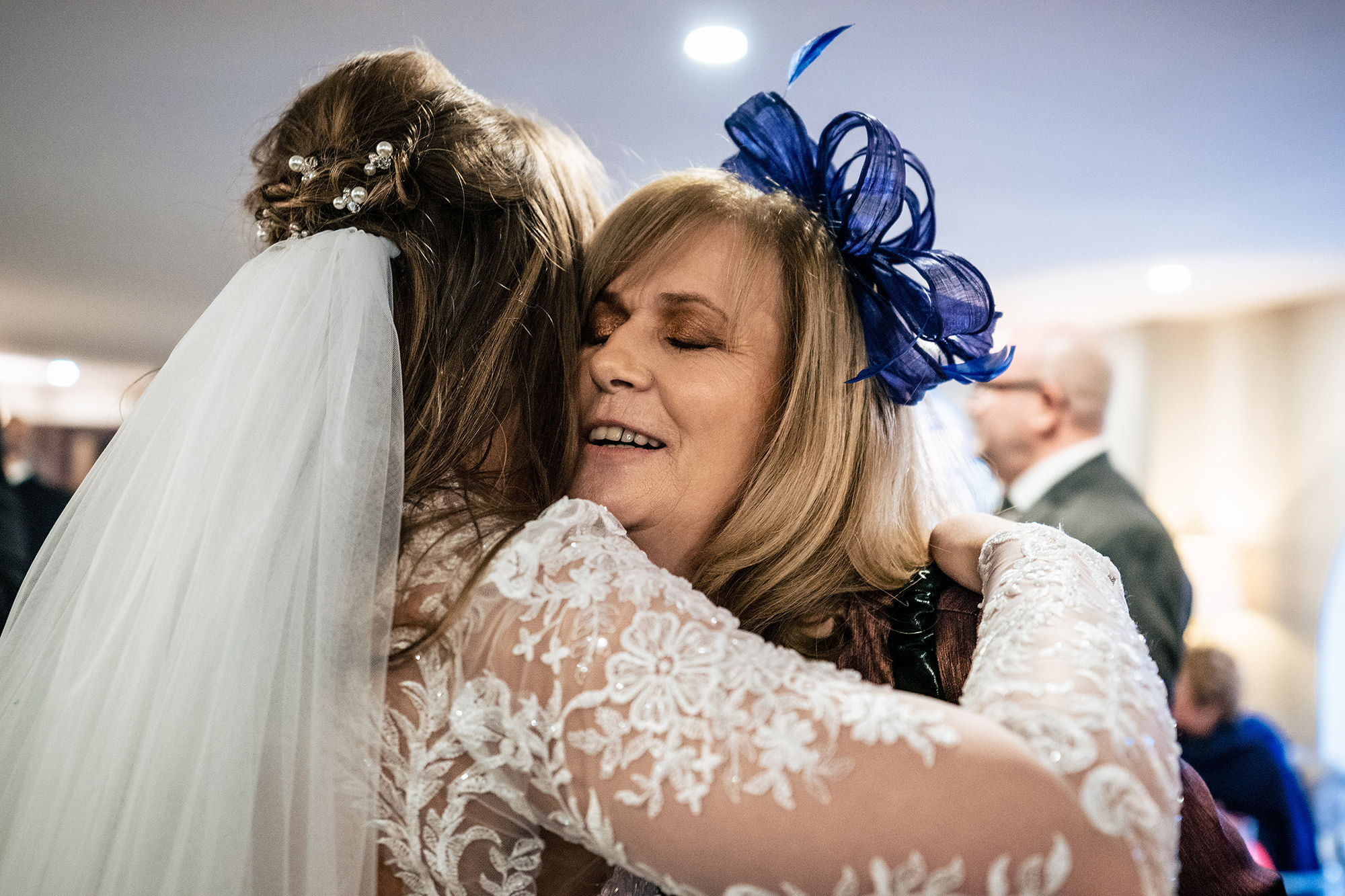 Abbie hugging a guest in a blue fascinator at the drinks reception, Merrydale Manor wedding photographer
