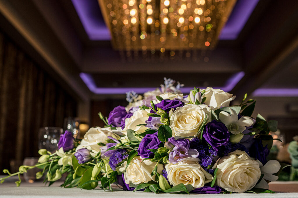 Purple and cream top table flowers under the chandelier in the Merrydale Manor reception room, Merrydale Manor wedding photographer