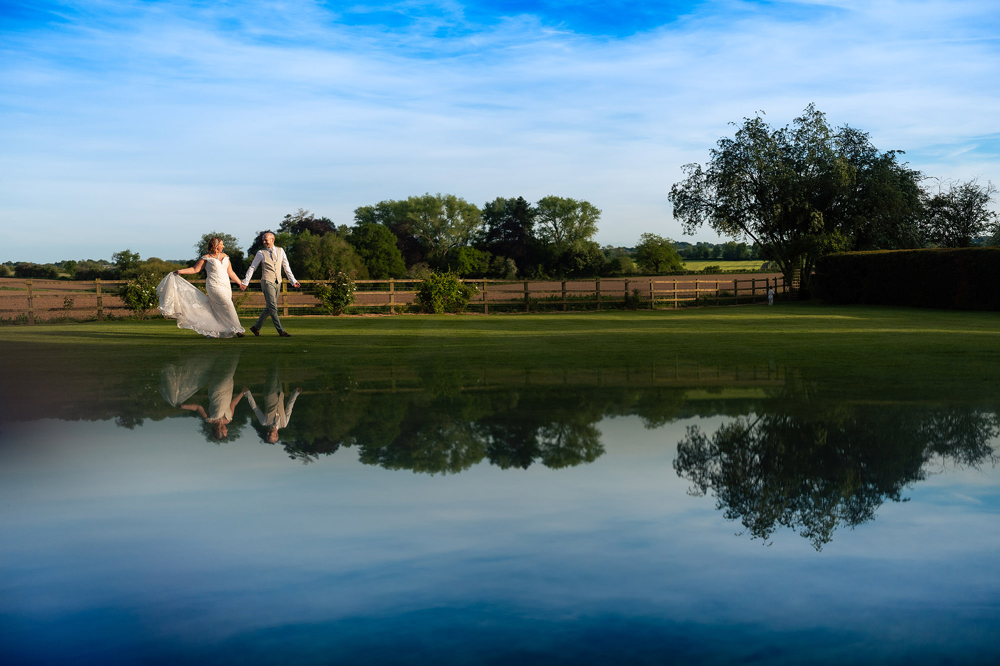 Bride and groom walking together over one of Helen’s mirrors in the grounds at Salt House as evening set in