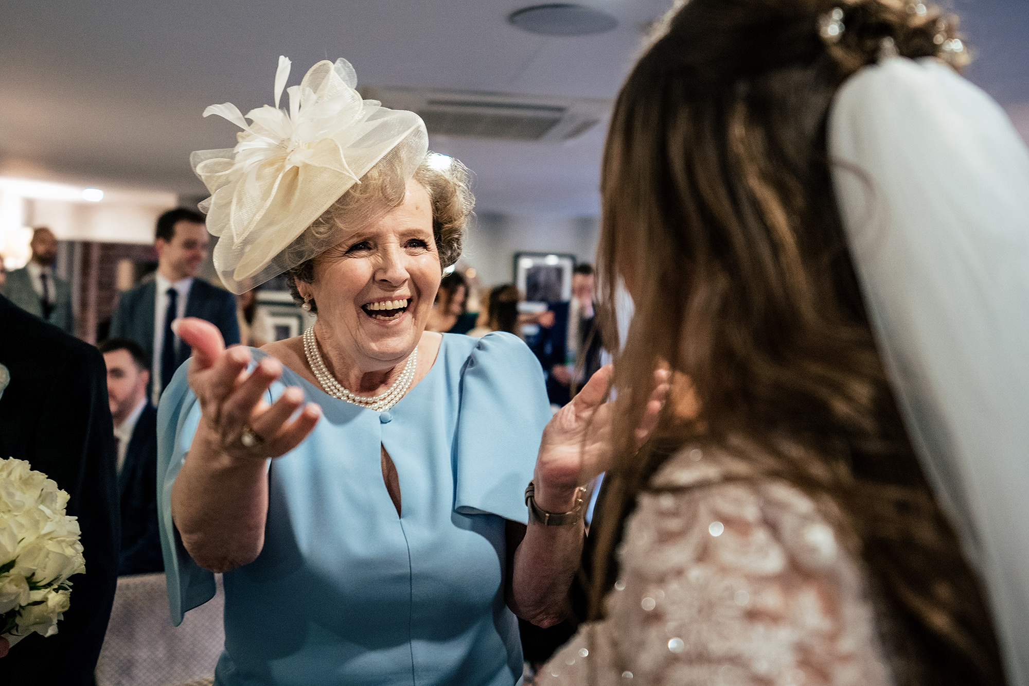An older guest in a cream hat beaming at Abbie during the drinks reception at Merrydale Manor