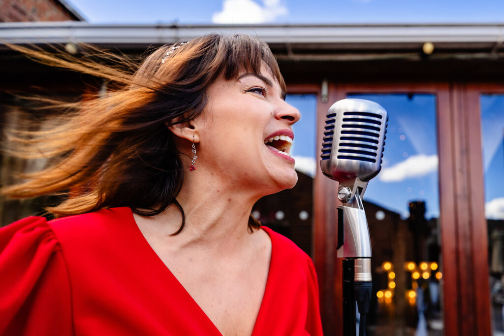 Singer in red singing into a vintage microphone outside, hair blowing, Nottingham wedding photographer