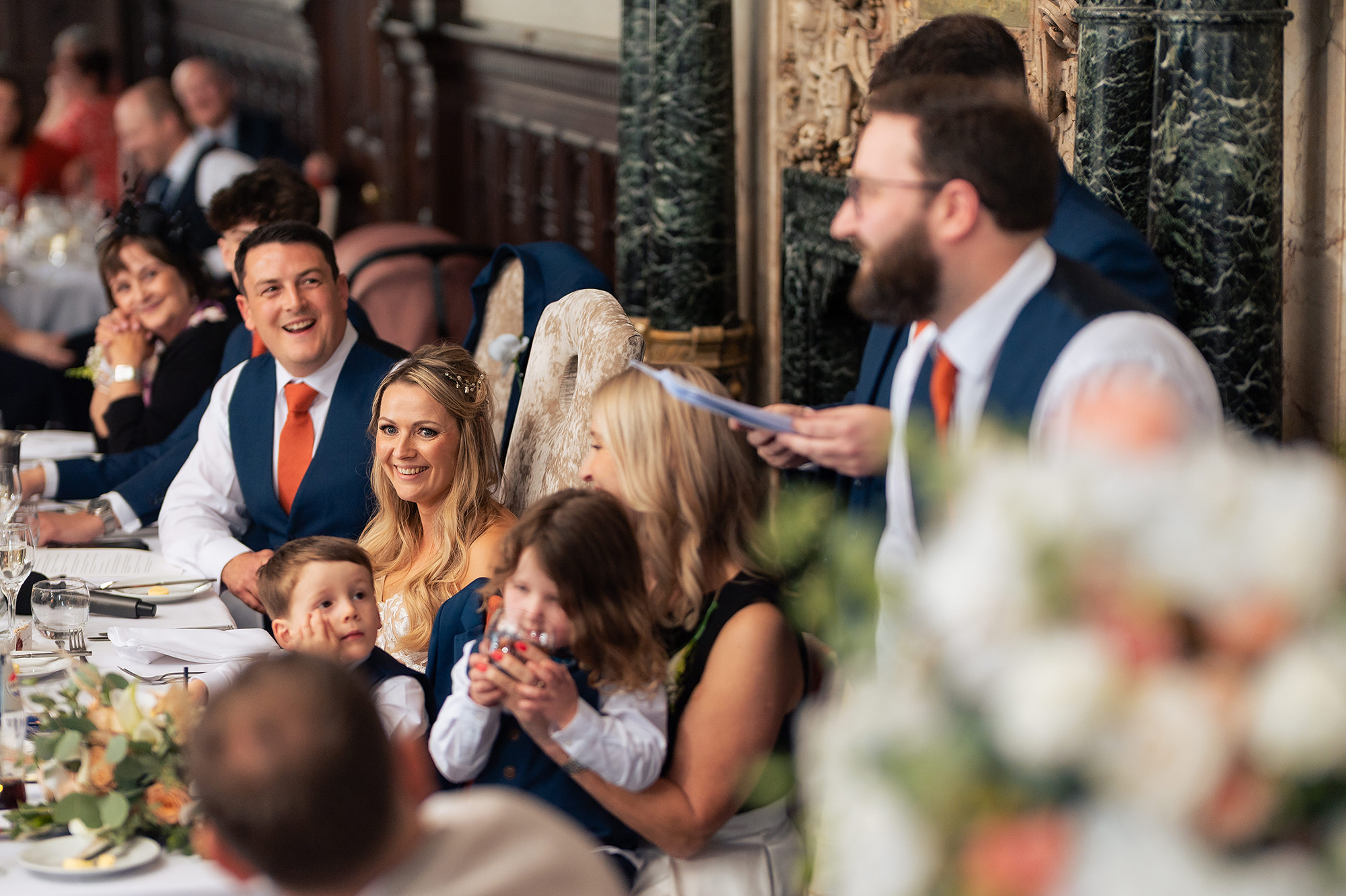 The bride laughing at the top table with a small child on her lap while a speech is read out