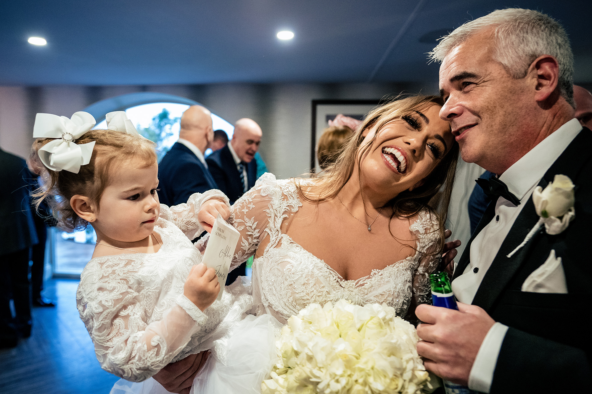 Abbie laughing with the littlest flower girl in her arms as a guest leans in at the drinks reception, Cheshire wedding photographer