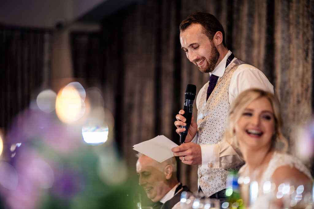 Groom giving his speech with the bride laughing beside him, Merrydale Manor wedding photographer