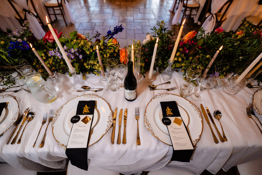 Table styling with gold cutlery, black and gold monogrammed menus, tall candles and bright florals, Swancar Farm wedding photographer