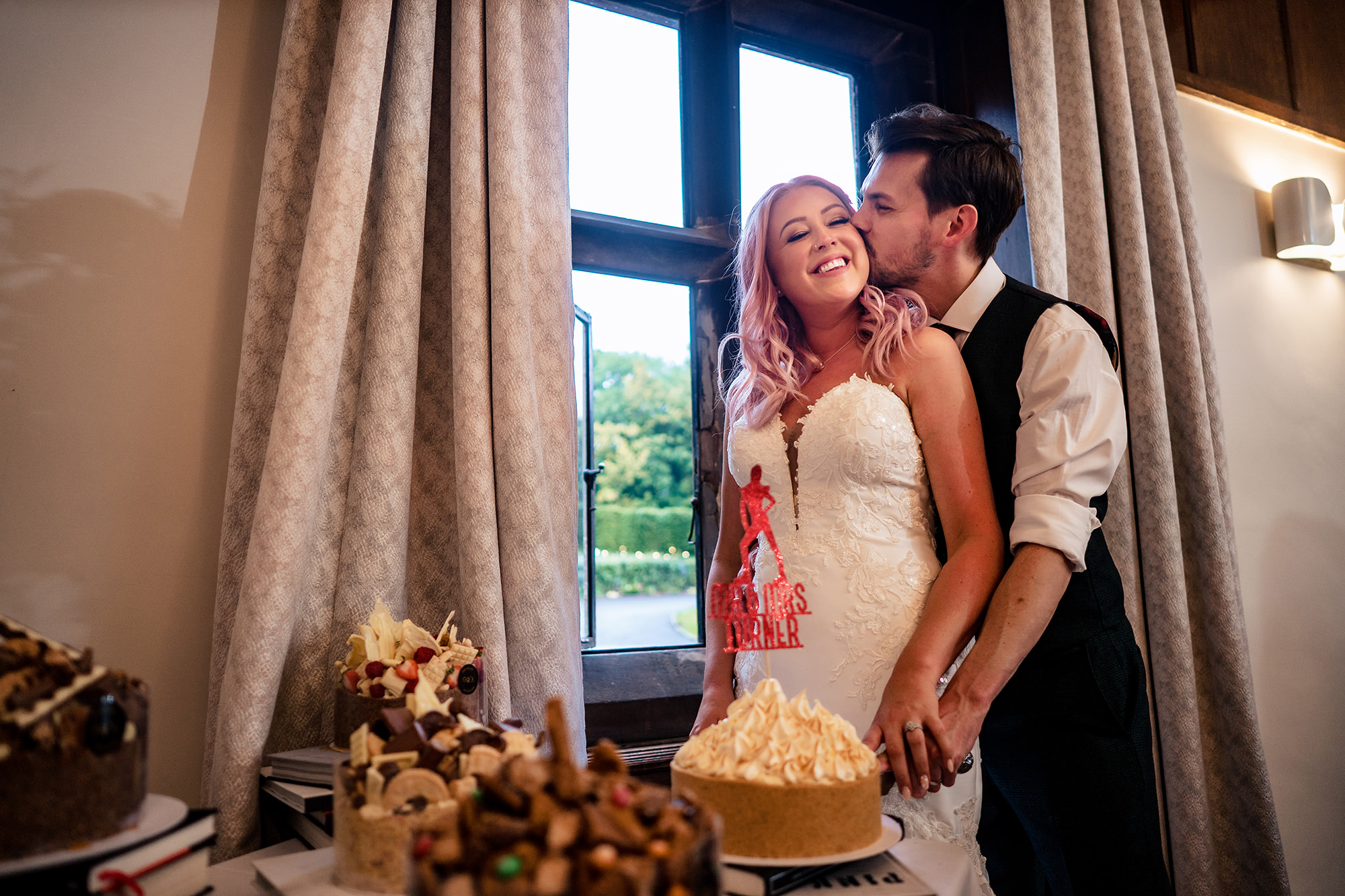 Groom kissing his bride as they cut their cake at Standon Hall
