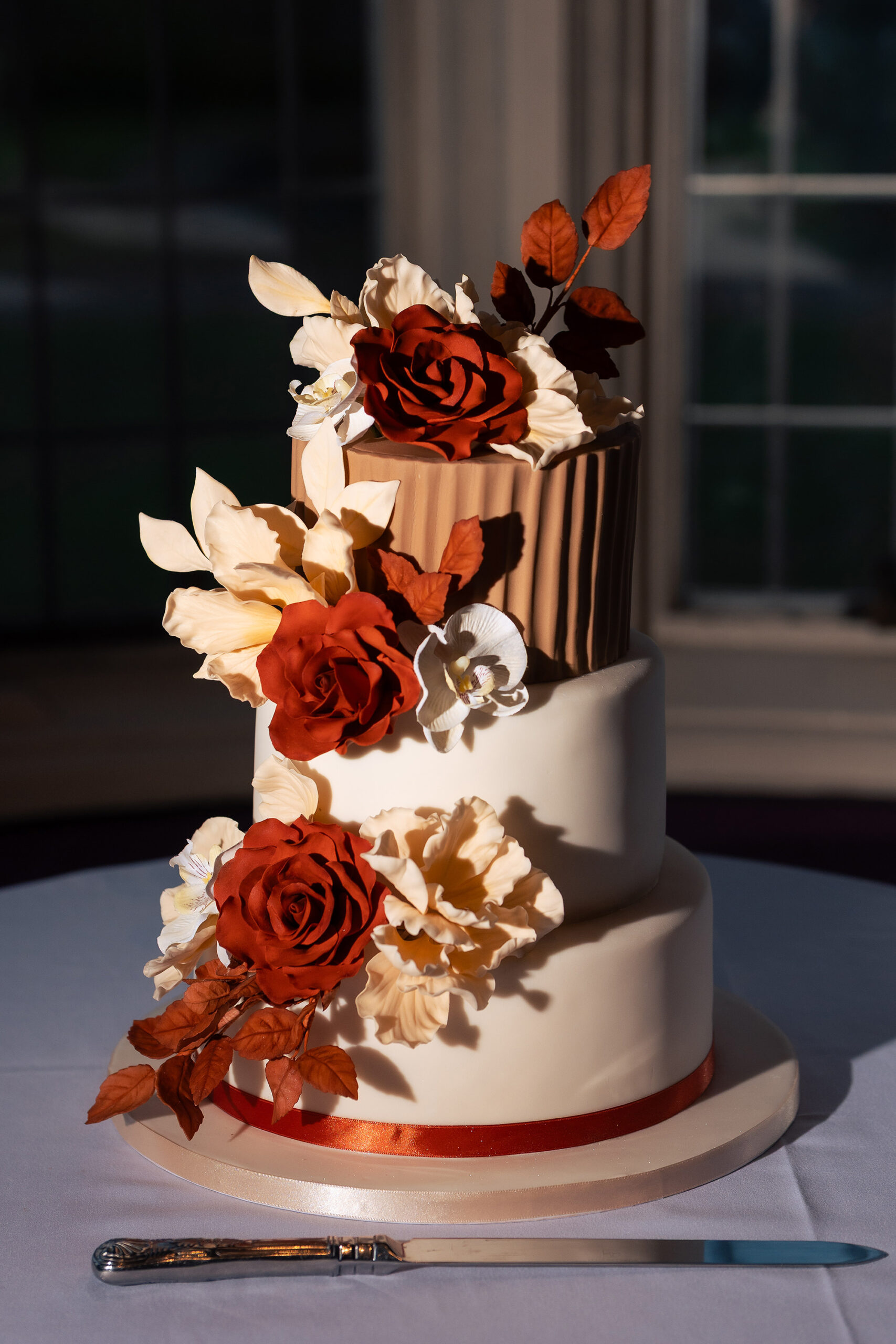 The three tier wedding cake lit dramatically against a dark window in the evening, knife laid beside it