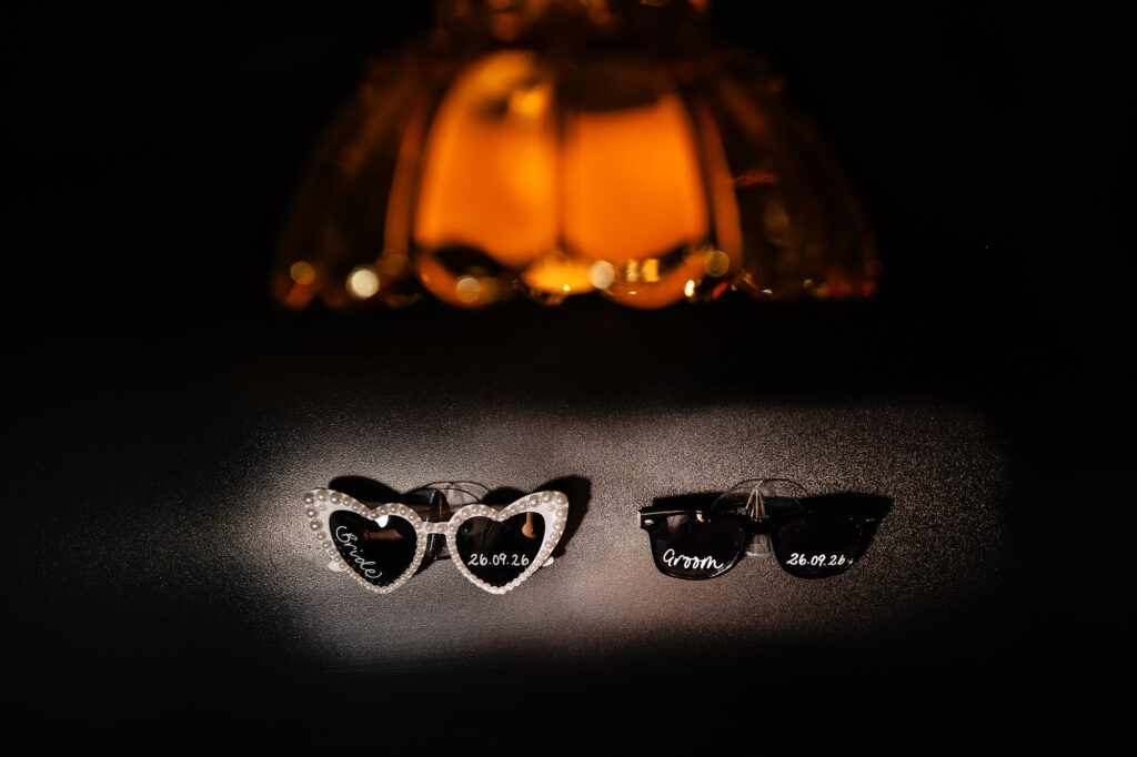 Two pairs of heart shaped sunglasses printed with names and the wedding date, lit under a lamp, Swancar Farm wedding photographer