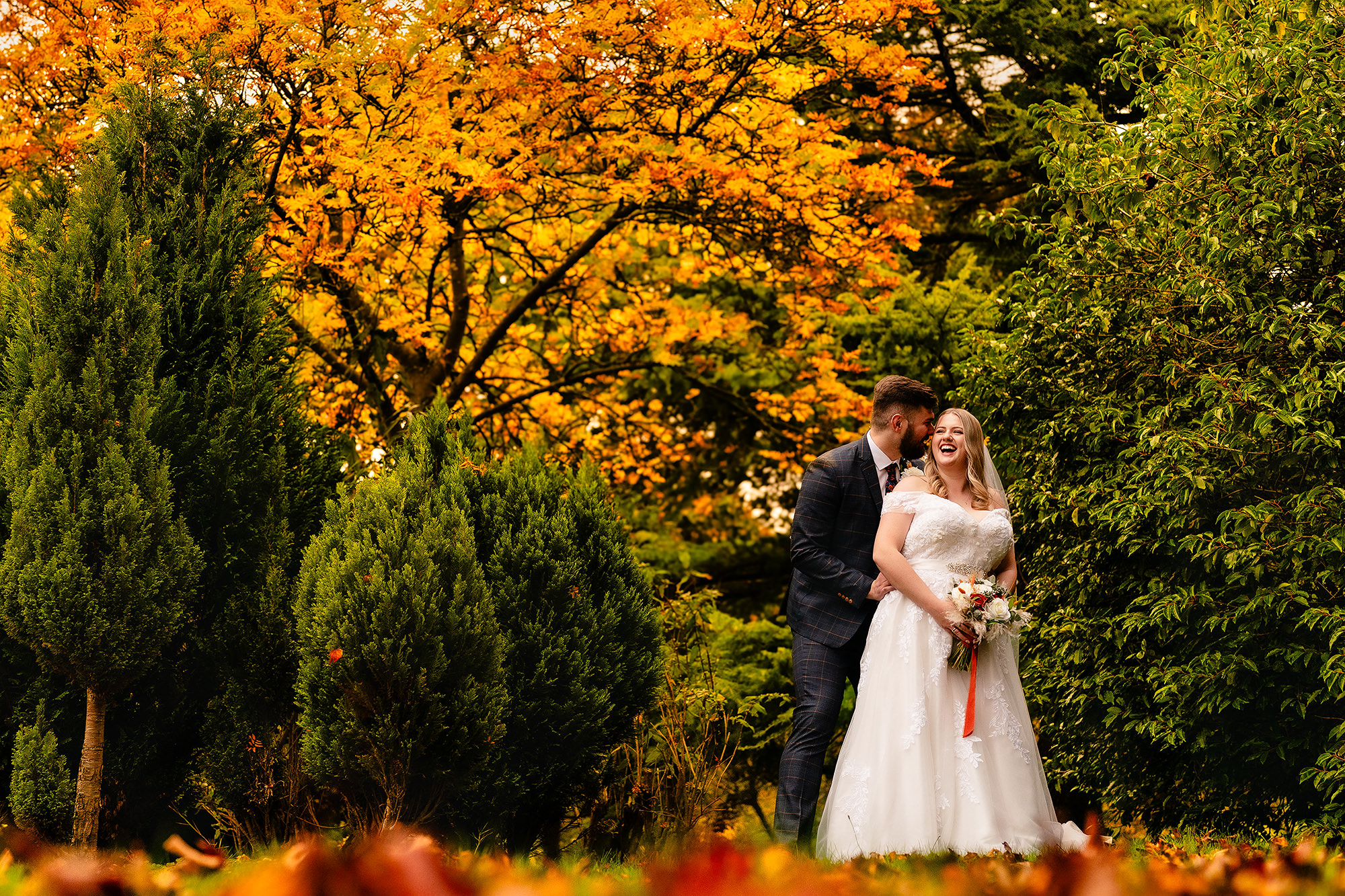 A wide portrait of the newlyweds among vivid orange autumn foliage at Crewe Hall, Cheshire wedding photographer
