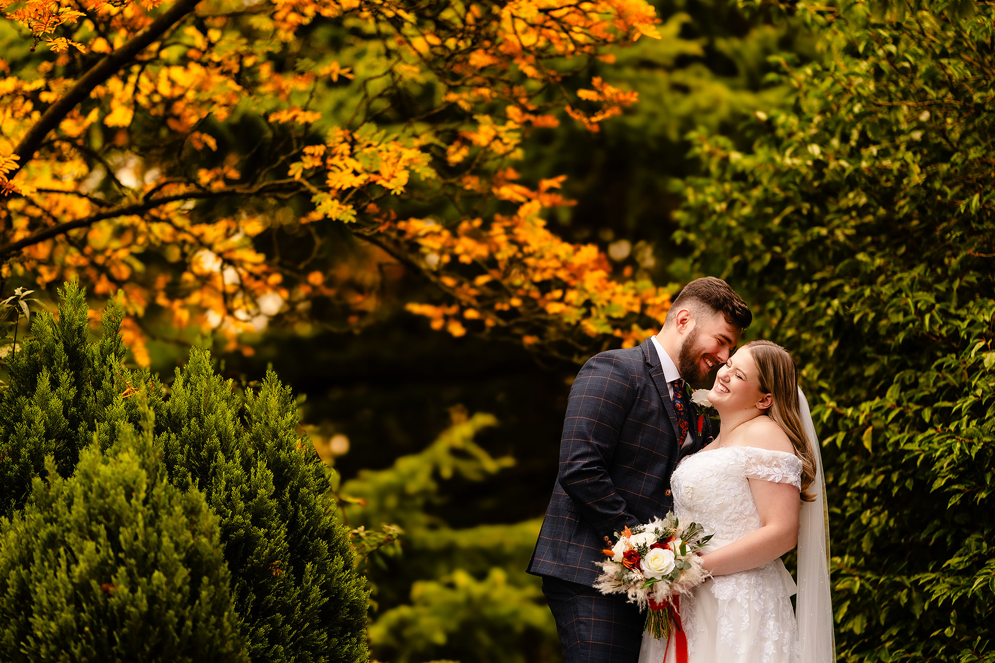Annie and Tom sharing a kiss among the autumn leaves at Crewe Hall, Cheshire wedding photographer