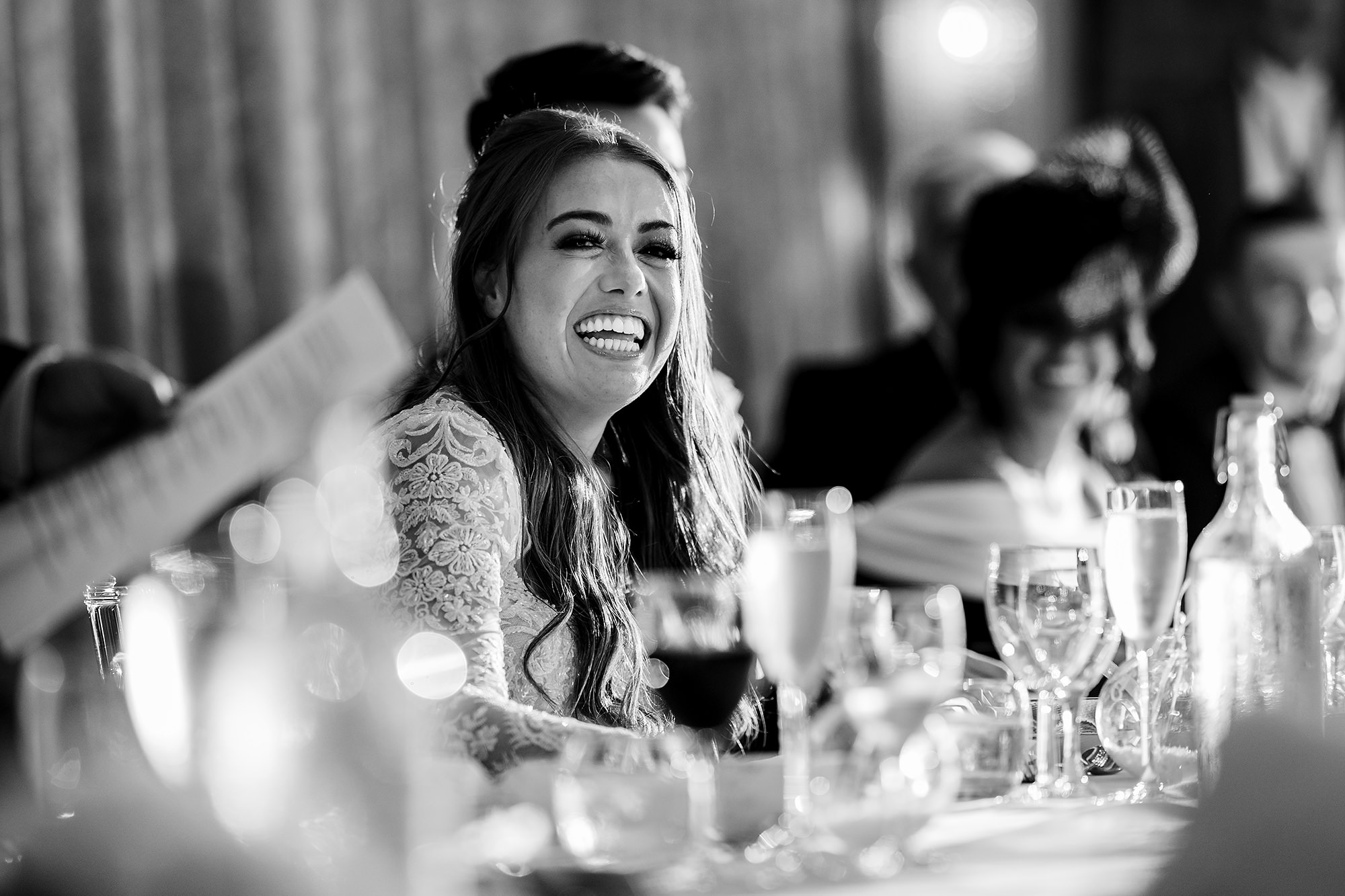 Black and white of Abbie laughing at the top table during the speeches at Merrydale Manor