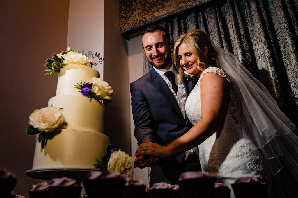 Bride and groom cutting their white three tier cake with cream roses, Merrydale Manor wedding photographer
