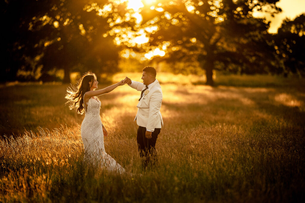 Tyrone twirling Gemma through long grass at golden hour, sun setting through the trees, Merrydale Manor wedding photographer