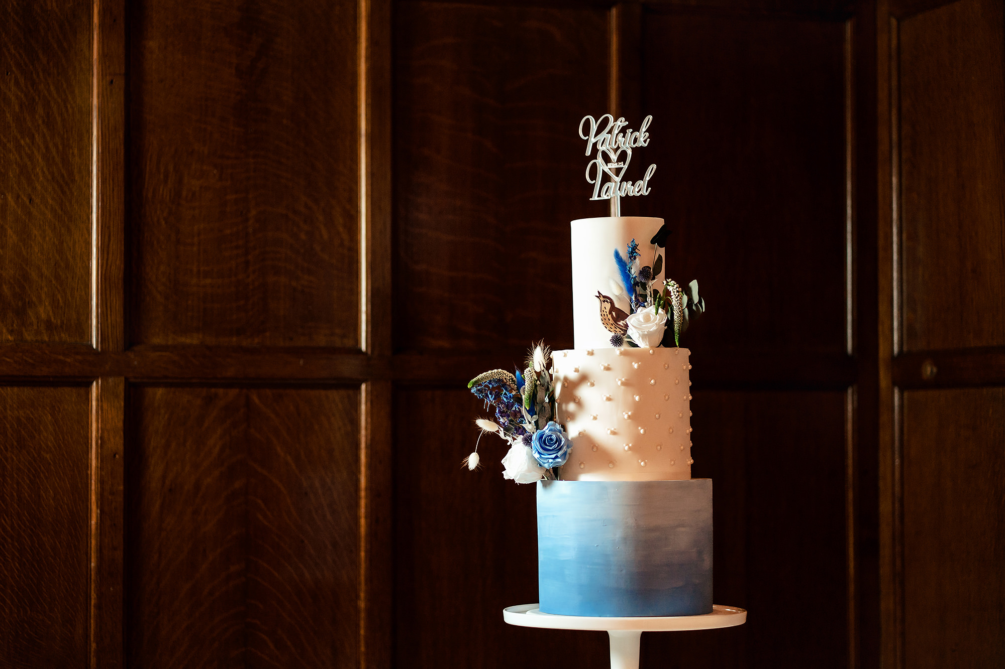 Three tier wedding cake with a blue ombre base and floral topper at Salt House, Staffordshire wedding photographer