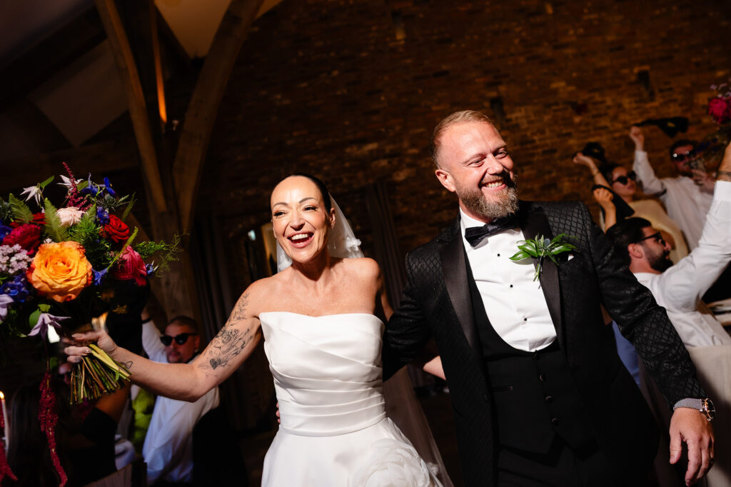 Kim and Glynn dancing into the wedding breakfast, Kim holding her bouquet up high, Swancar Farm wedding photographer