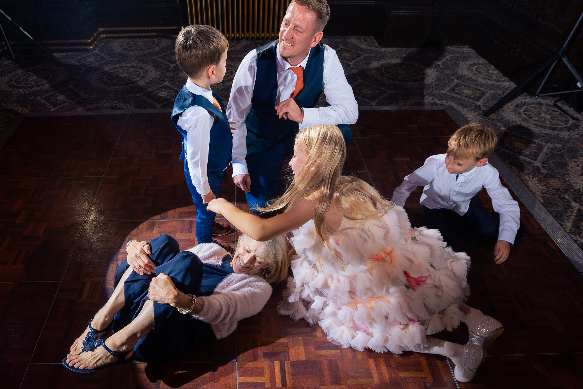The bride sitting on the parquet dance floor surrounded by children in a heap of skirts and laughter