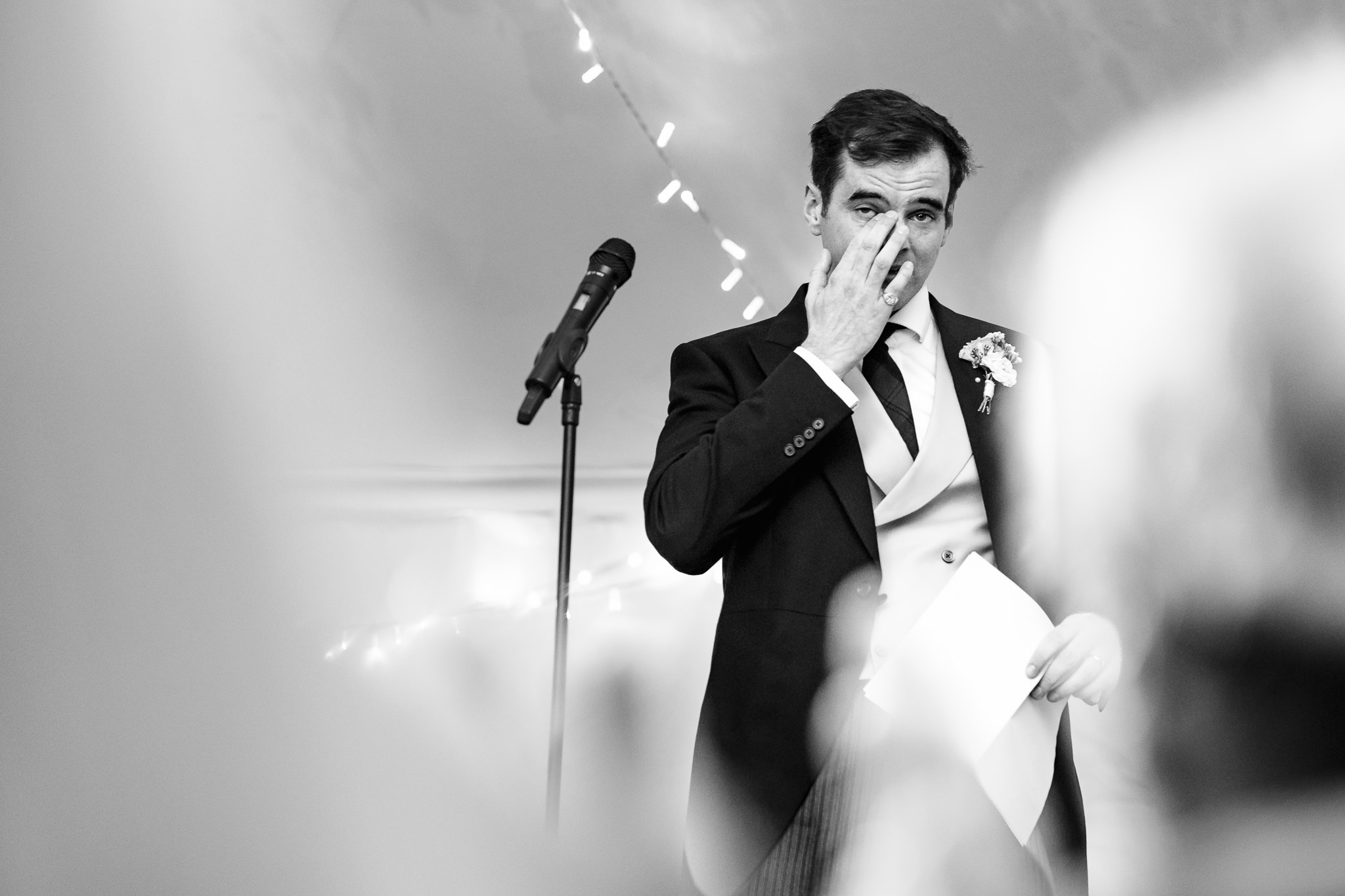 Black and white photograph of a speaker wiping his eyes during the wedding speeches