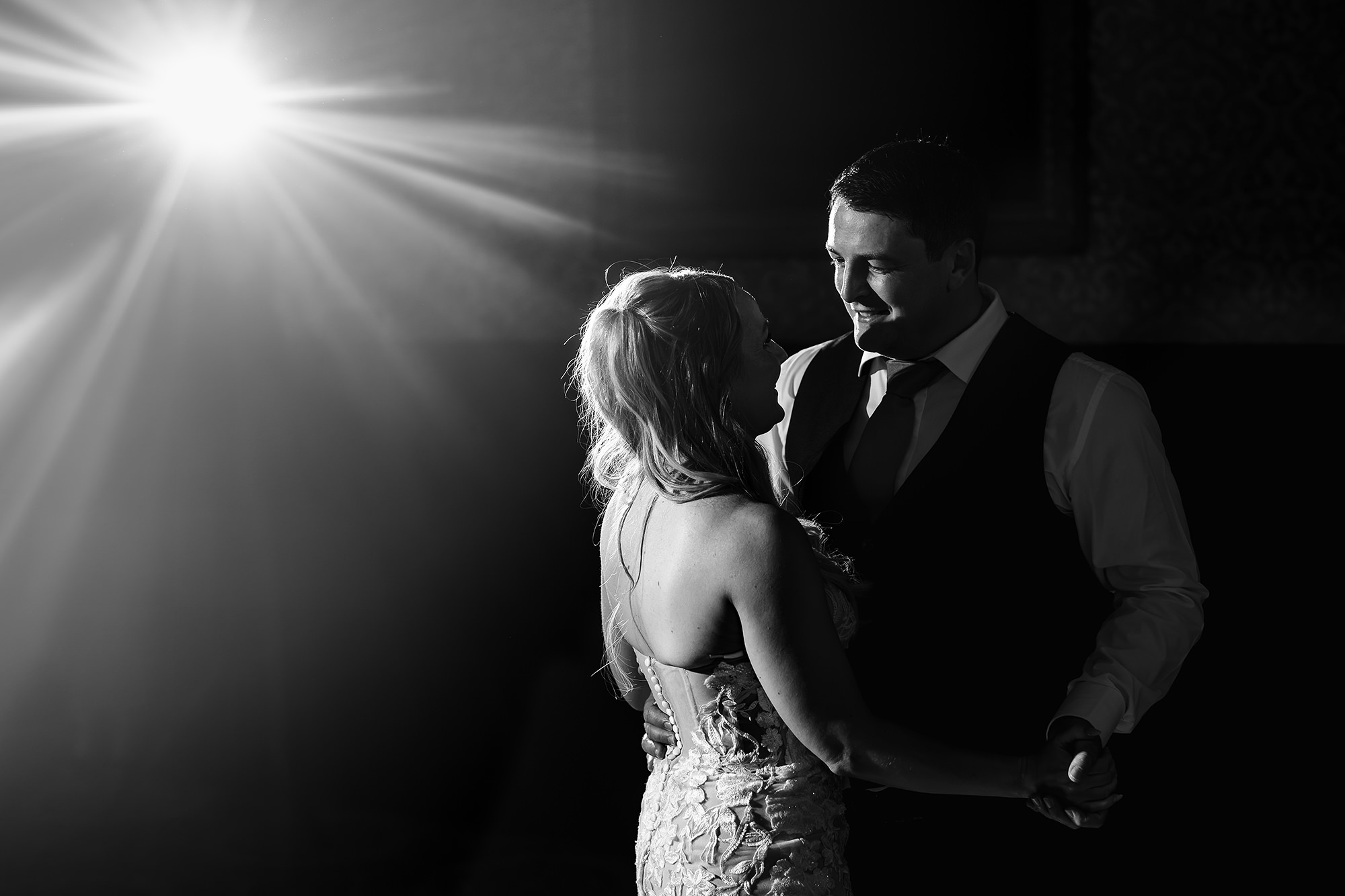 Black and white photograph of Lauren and Dan during their first dance, a burst of light flaring behind them
