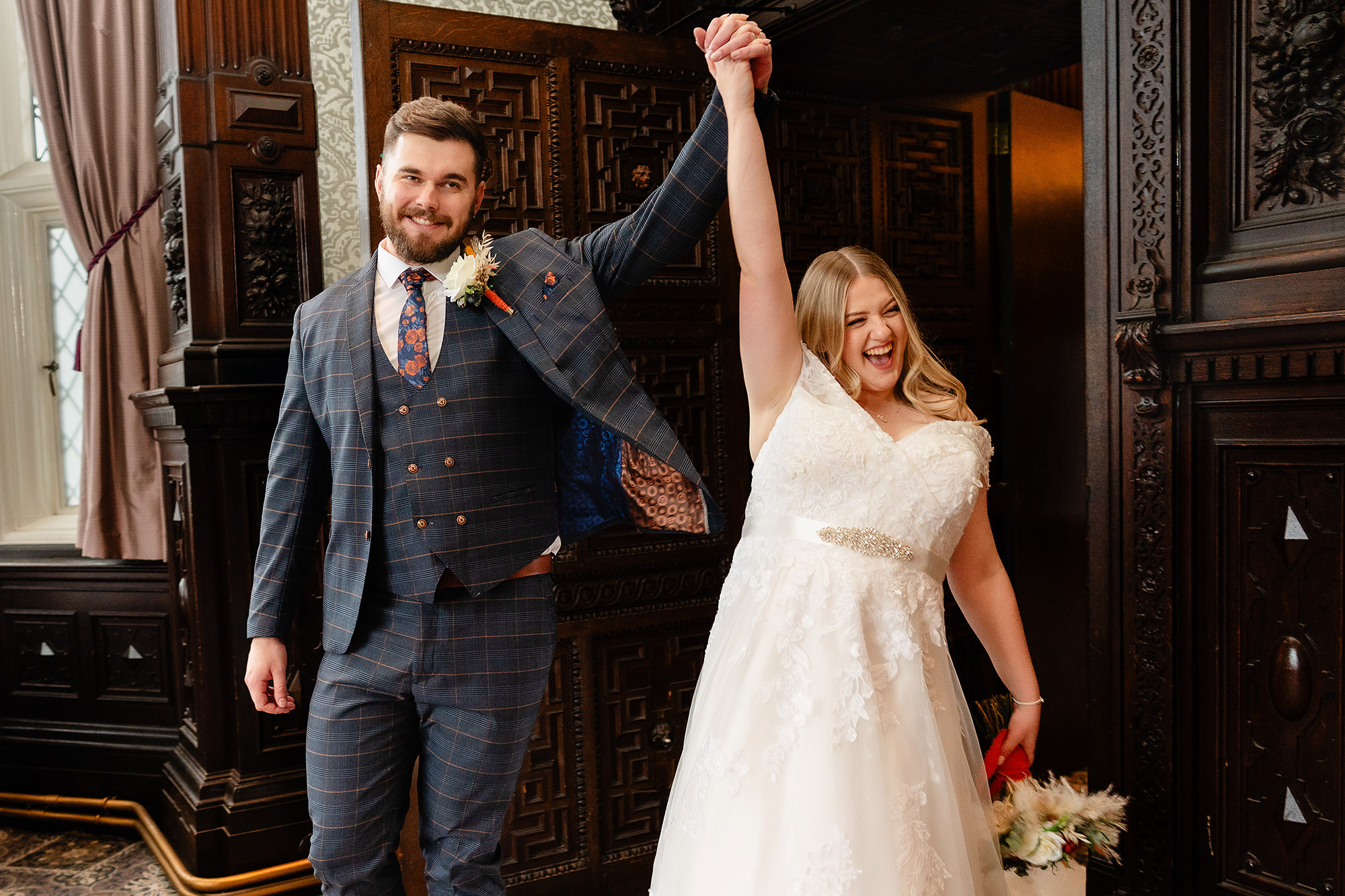 Tom raising Annie’s hand triumphantly in one of Crewe Hall’s candlelit hallways, Cheshire wedding photographer