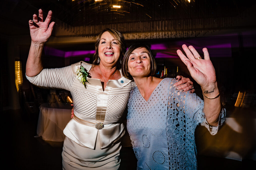 Two women dancing with their arms in the air on the dance floor, Cheshire wedding photographer