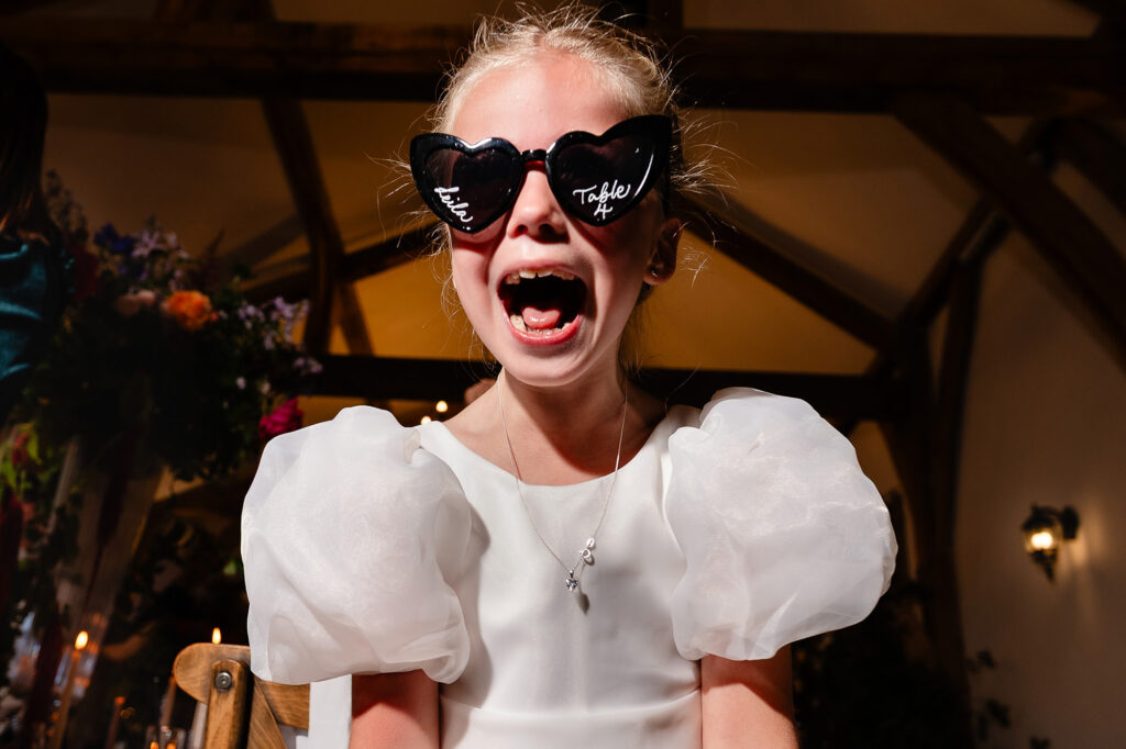 Flower girl shouting in personalised heart shaped sunglasses, Nottingham wedding photographer
