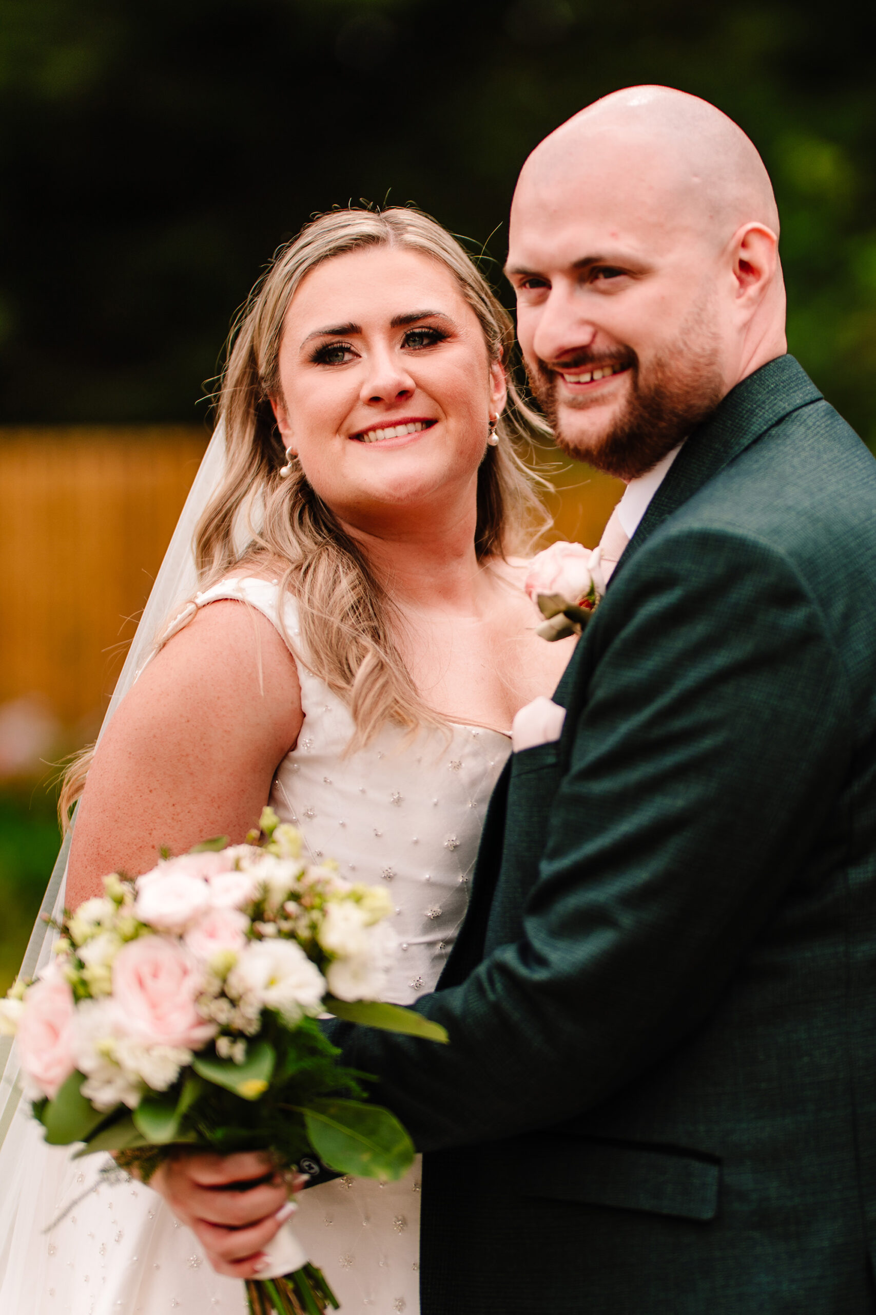 Chloe and Pete close together in the Wrenbury Hall gardens with her bouquet