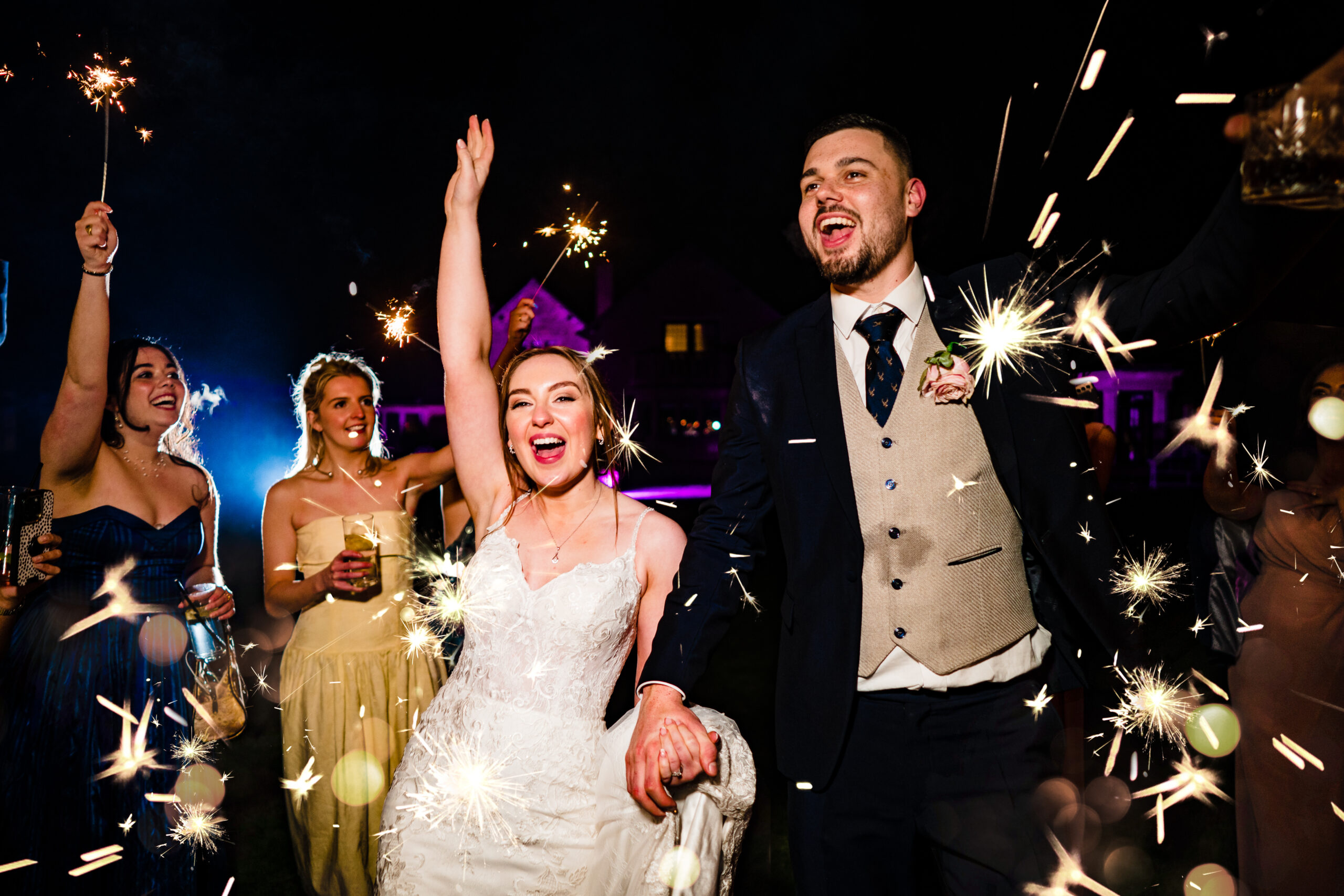 Bethany with her arm in the air and Dean cheering as guests wave sparklers outside