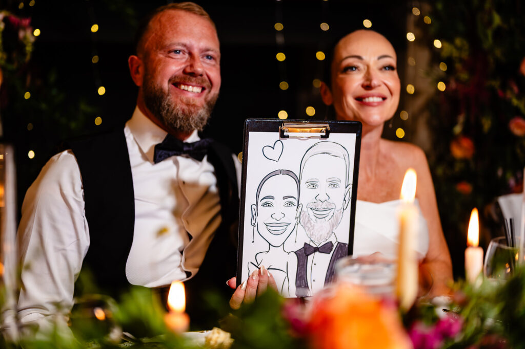 Glynn and Kim at the top table holding up a caricature of themselves, Nottingham wedding photographer