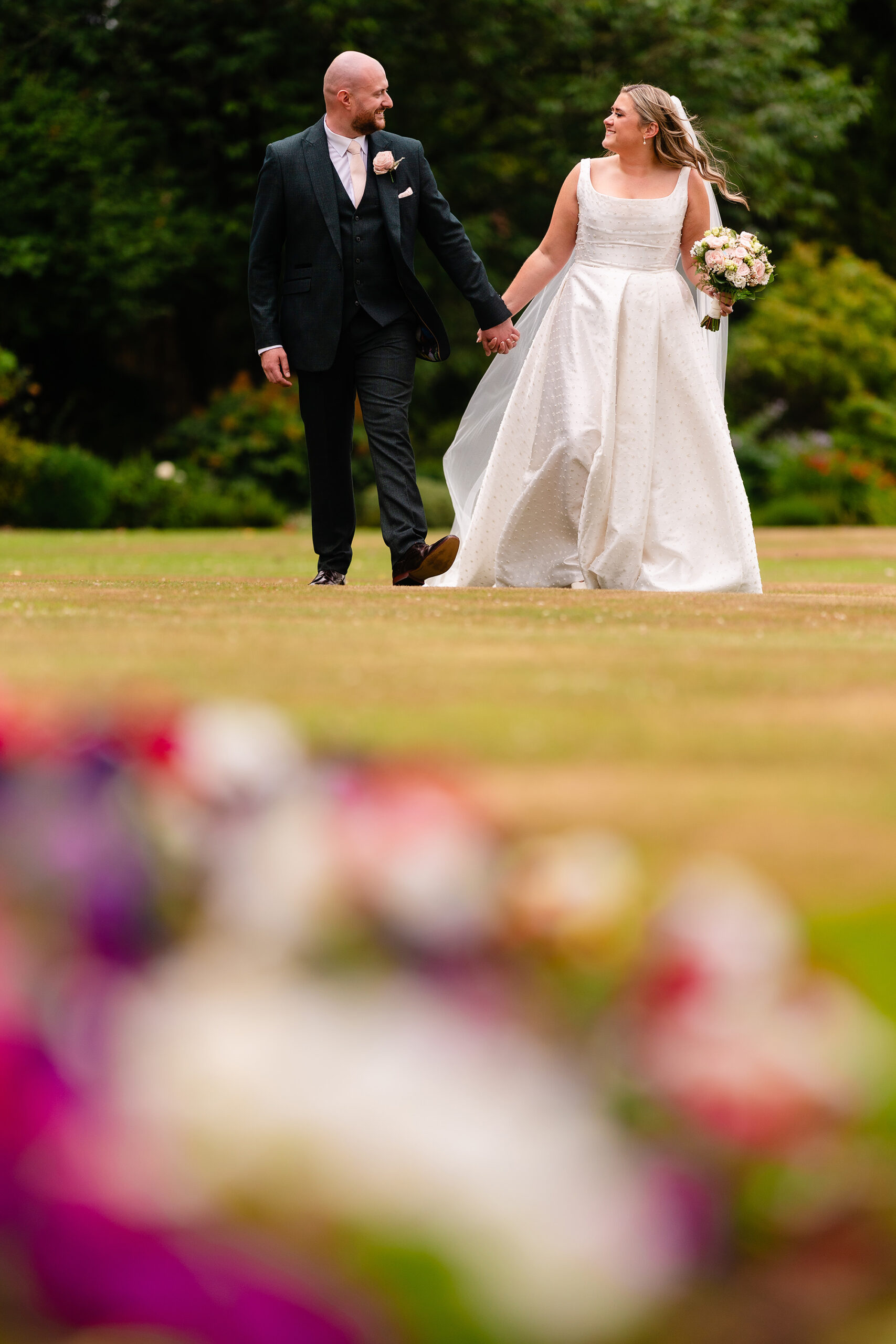 Chloe and Pete walking together, her bouquet blurred in the foreground
